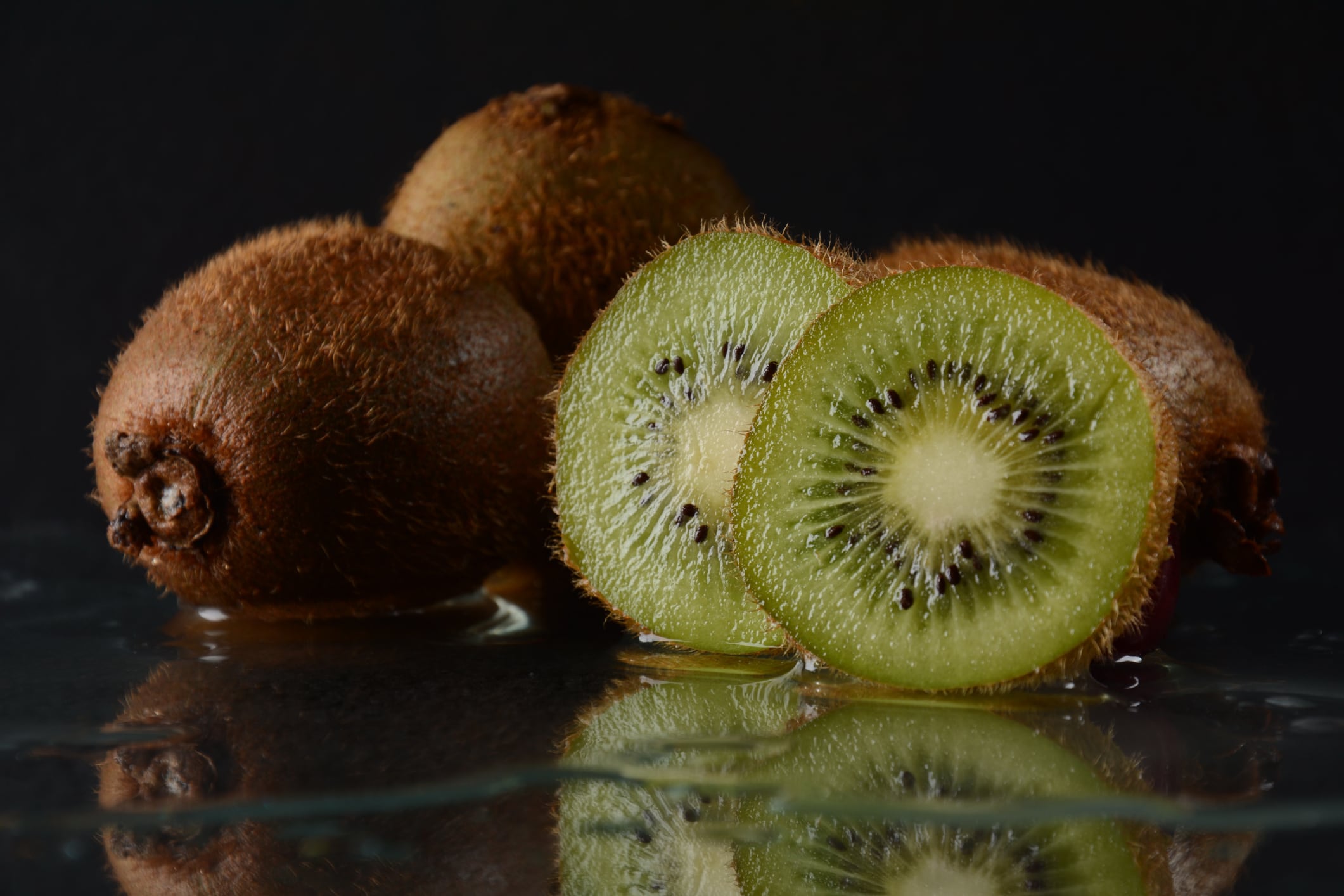 Kiwi slices on a black reflective glass surface. Kiwi on black glass