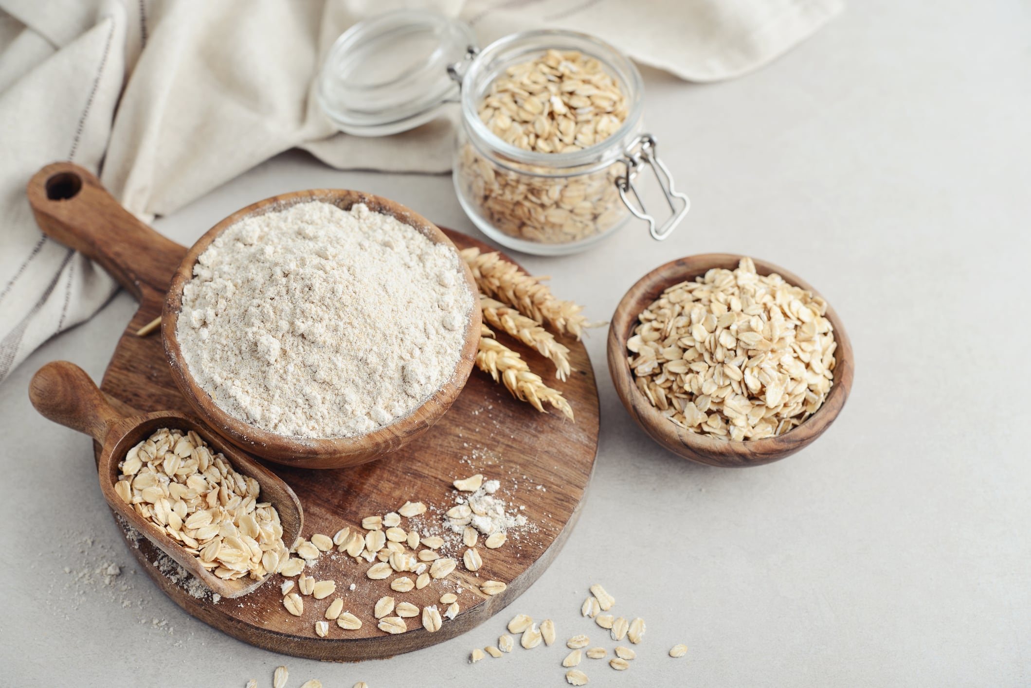 Oat flour in wooden bowl with raw oatmeal on light background, closeup