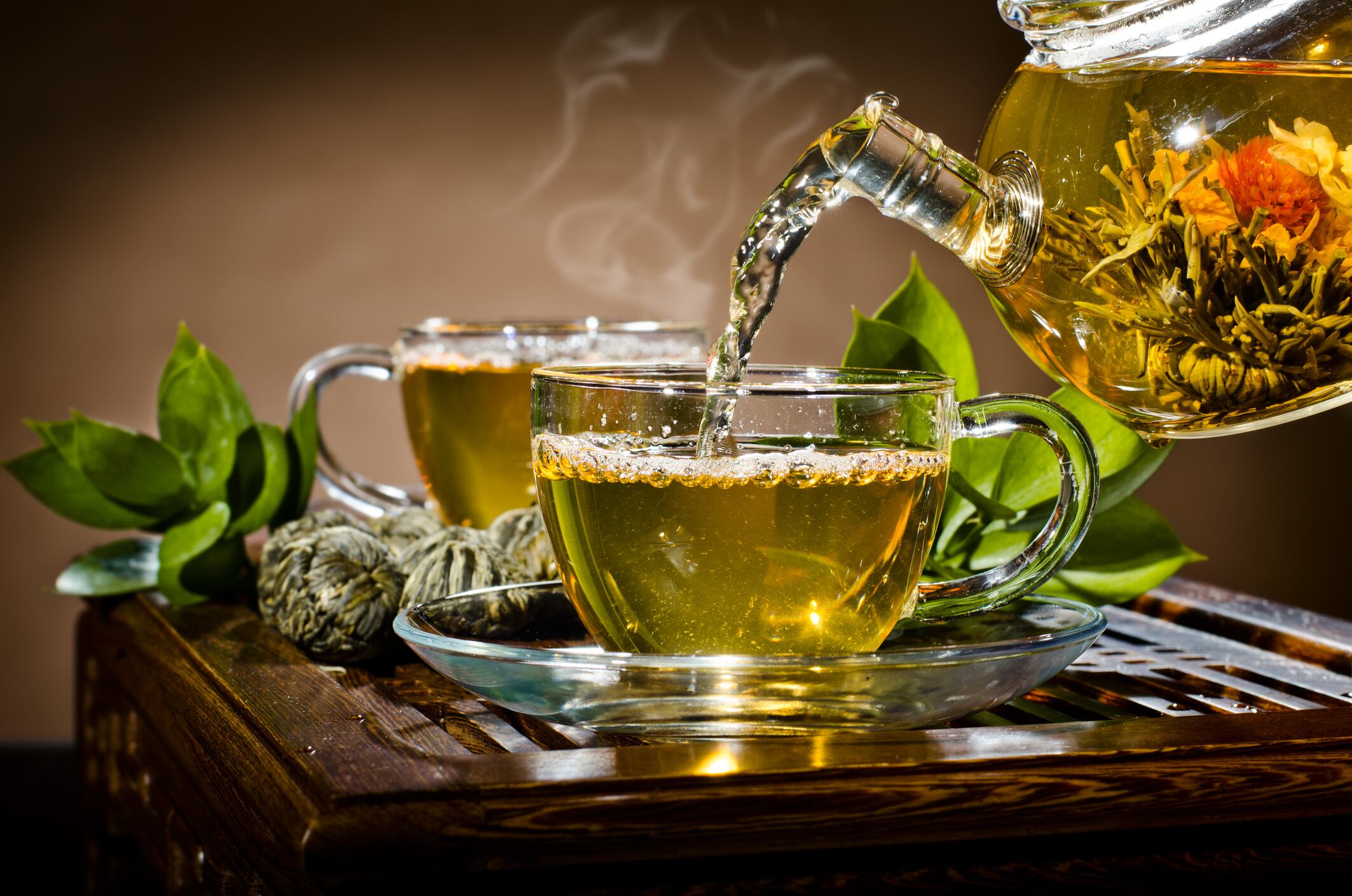 horizontal photo, of the glass teapot flow green tea in cup on brown background,  tea ceremony
