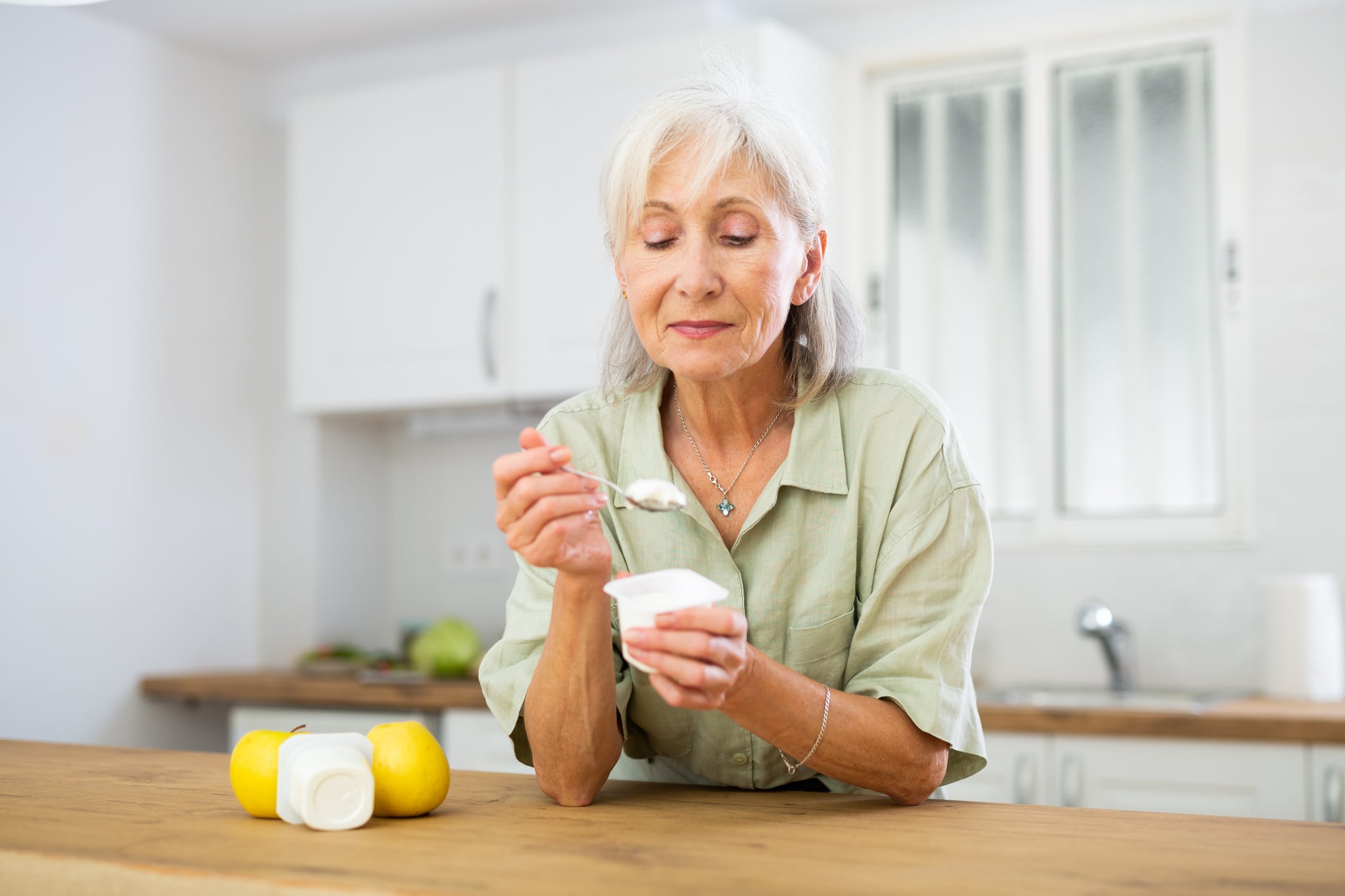 Portrait of smiling retried woman enjoying yogurt as healthy snack in home kitchen