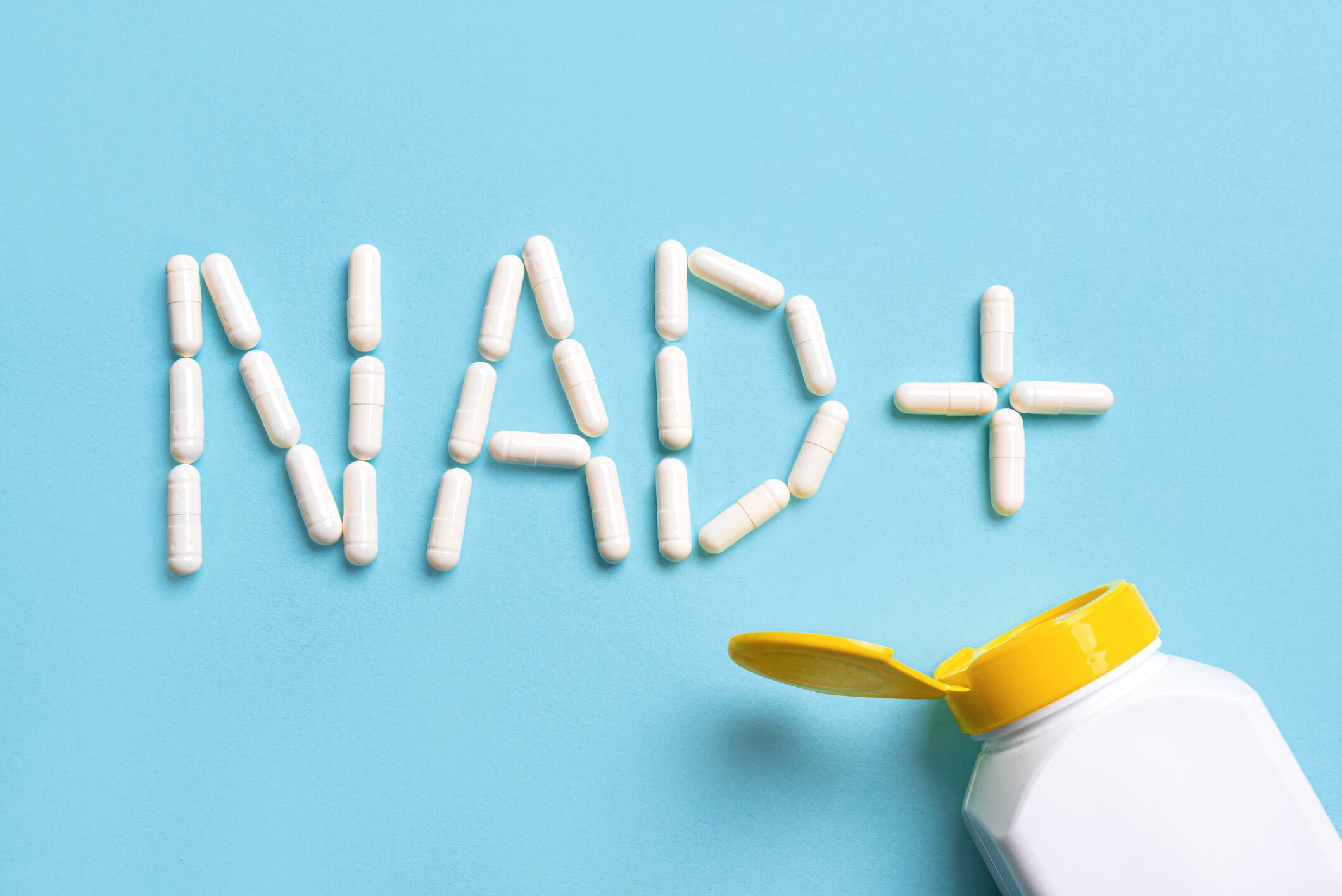 NAD+ supplement pills for anti-aging and biohacking on blue background, top view. Letters NAD plus capsules.
