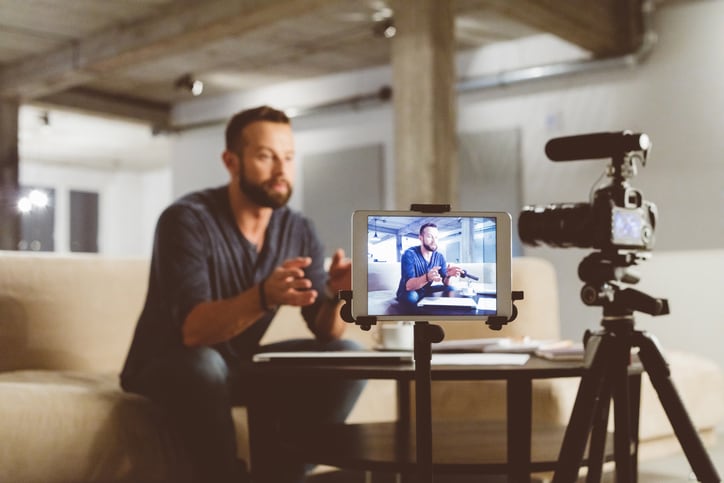 A young male influencer records a video blog for Instagram with a digital camera, talking to his audience about nutritional supplements.