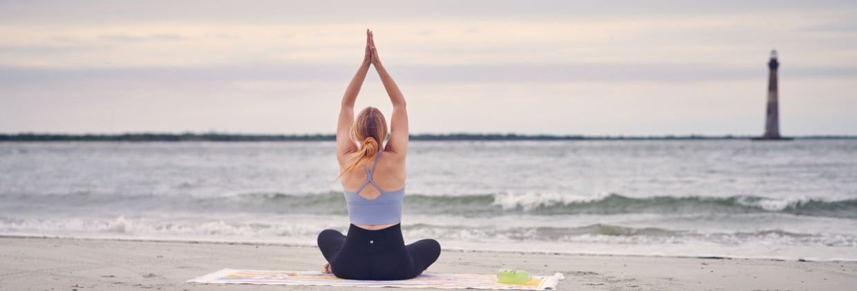 Woman with Sports Drink Meditating at Beach with Lighthouse