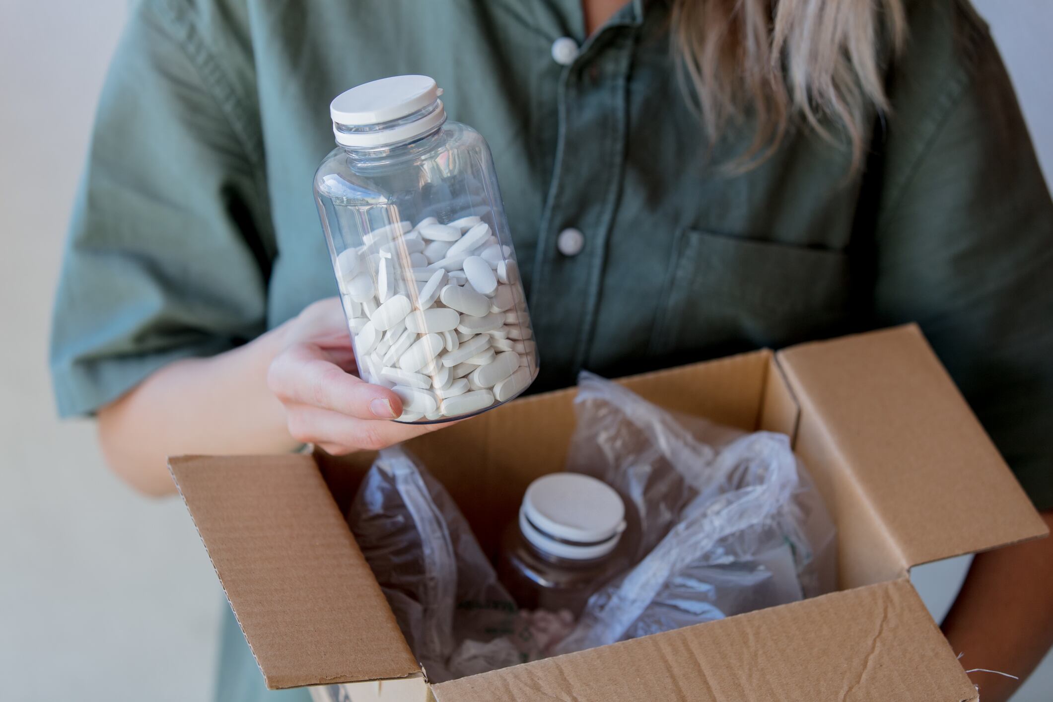 woman pulls a jar of pills out of the box