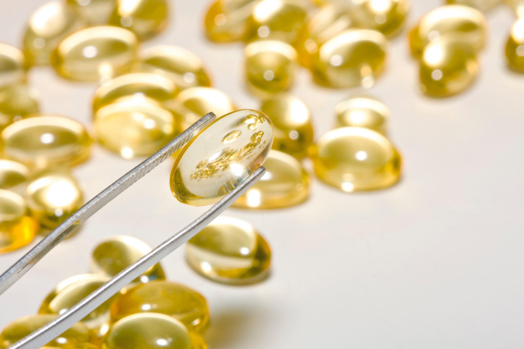 vitamin E and cod liver oil capsules on the tip of tweezers.Nutritional supplement pills in yellow and shallow depth of field.