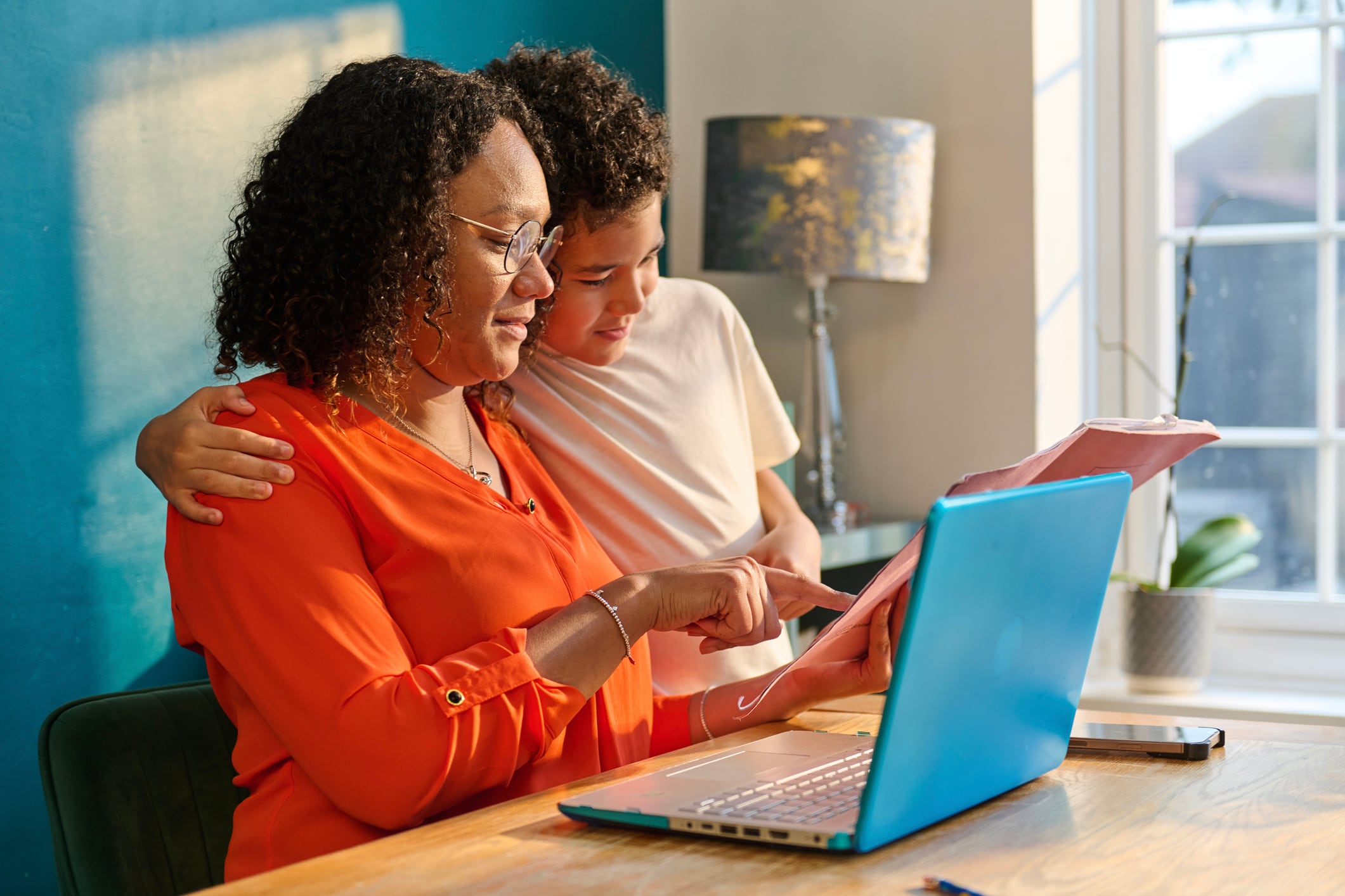 Mother and son close together reviewing homework at the dining table. Warm family moment showing support, learning and everyday parenting.
