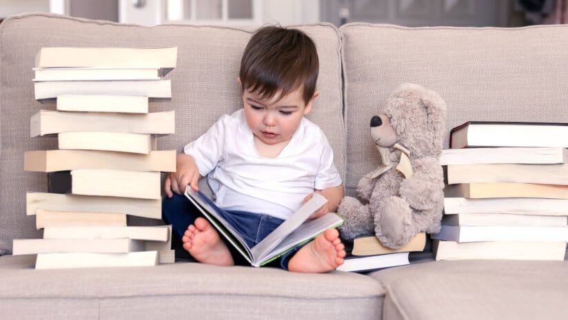 Child reading piles of books with teddy bear