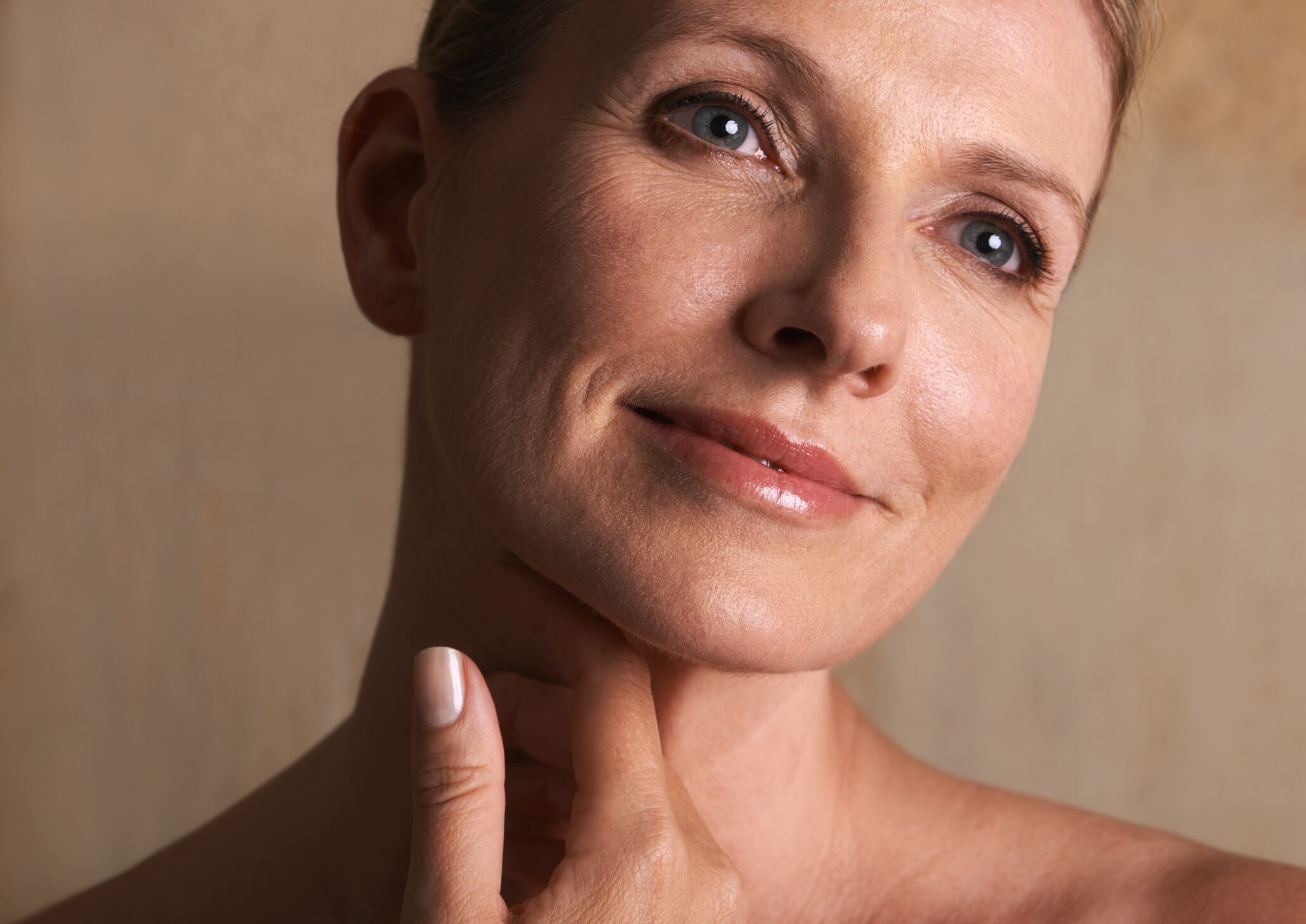 A mature woman with bare shoulders looking away against a beige background