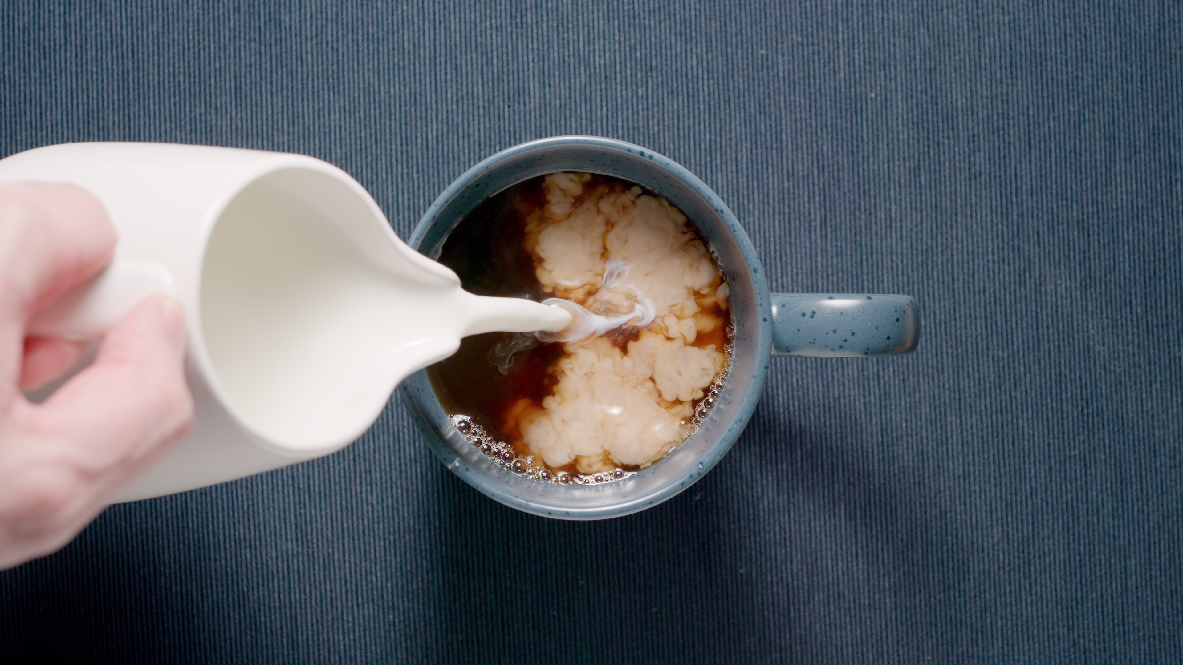 TOP VIEW: Adding cream to a blue cup on a table. Milk coffee. Dark blue.