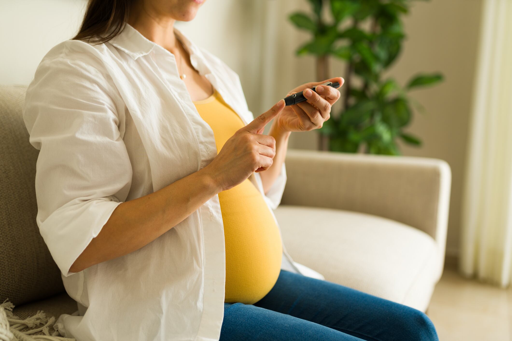 Close up of a caucasian pregnant woman sick with diabetes checking her blood sugar levels using a monitor on her finger