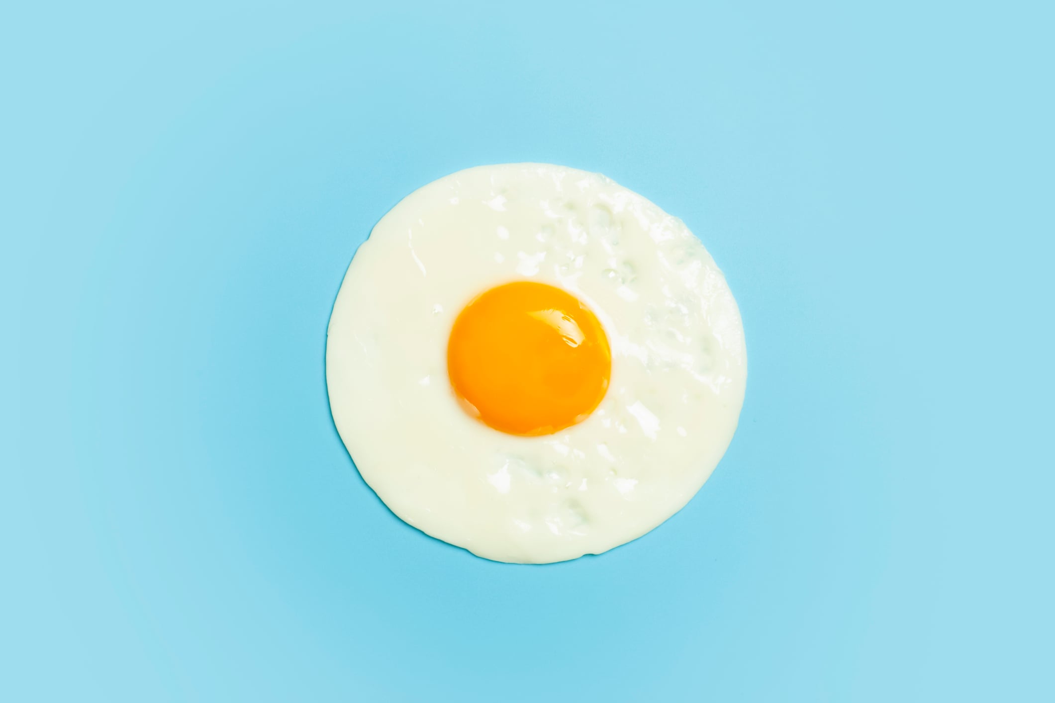 Fried egg is minimal. Fried egg isolate on a blank color light blue background. Creative breakfast and food idea. High quality photo