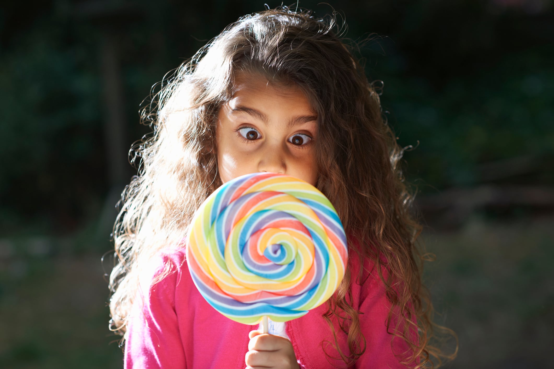 Portrait of girl crossing eyes with lollipop in front of her face in garden