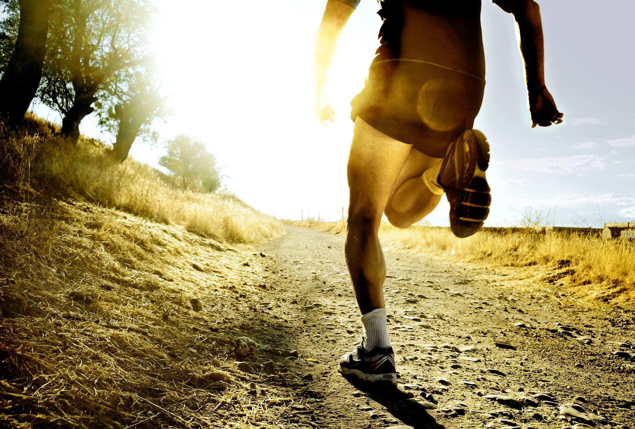 close up silhouette legs and feet of extreme cross country man running and training on rural track jogging at sunset with harsh sunlight and lens flare in countryside sport and healthy lifestyle concept