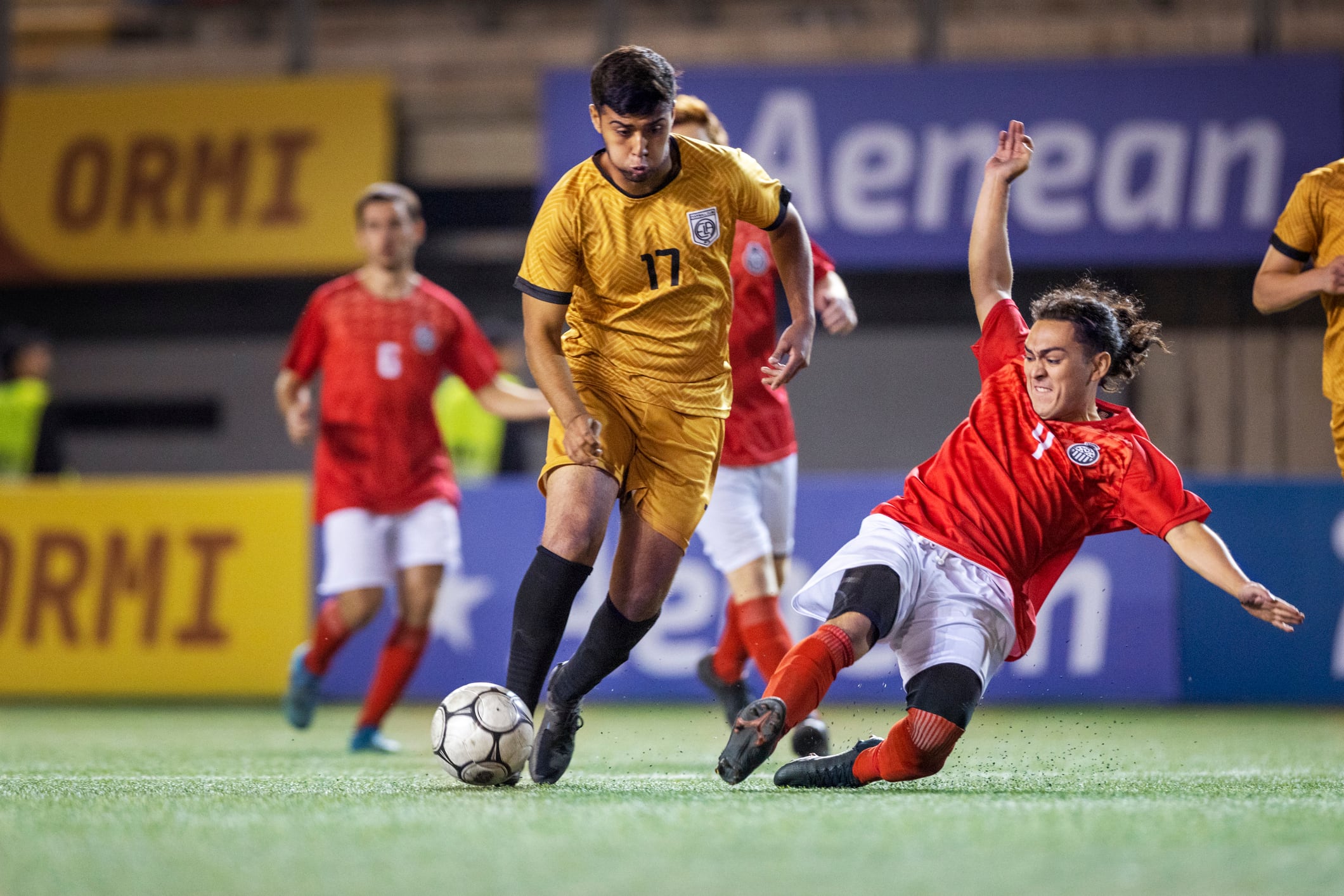 Adult male football holding midfielder intensely slide tackles his rival player in an attempt to steal the soccer ball as his opponent side steps him trying to avoid the tackle during an influential championship match