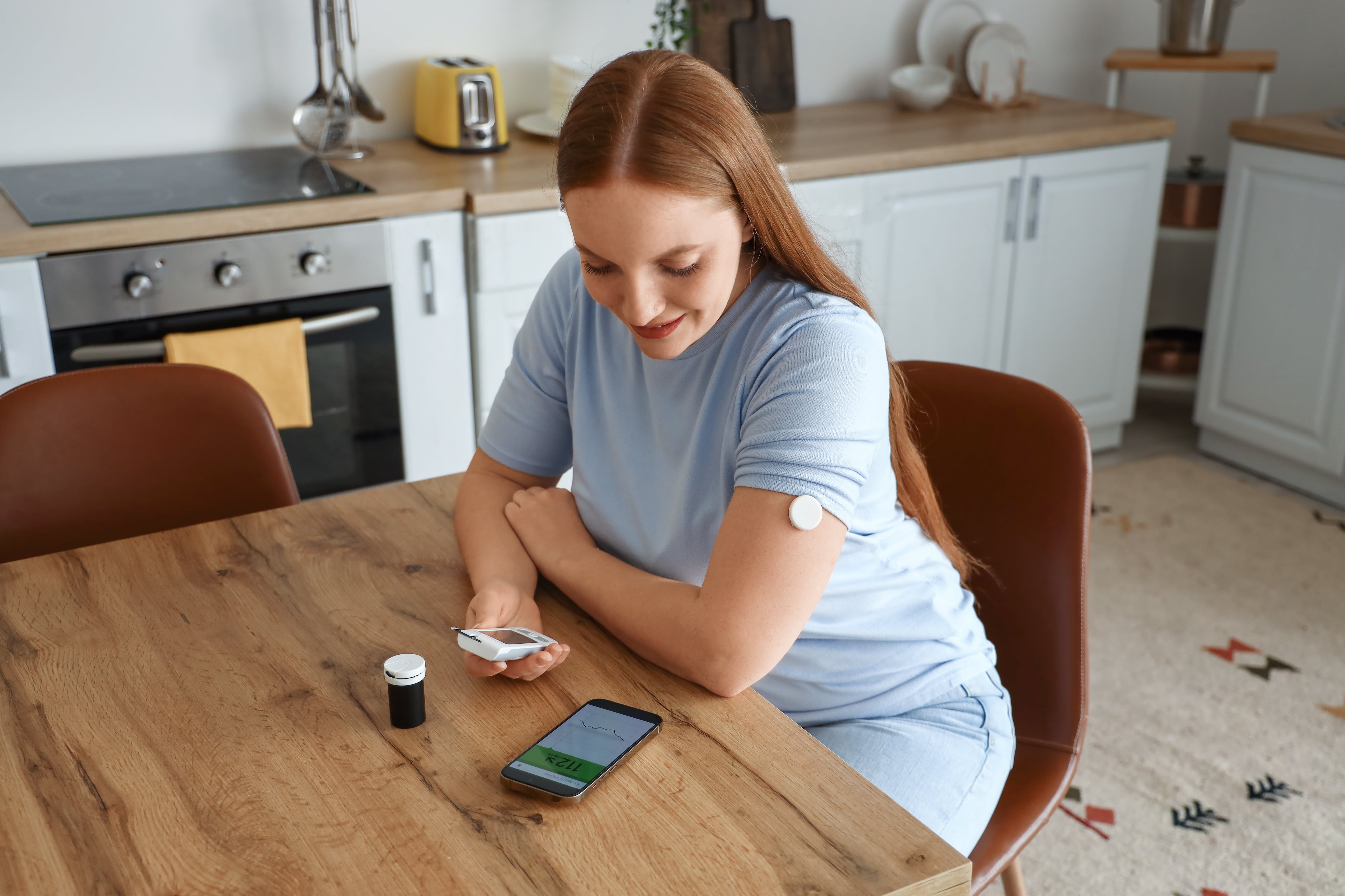 Woman with glucose sensor using mobile phone for measuring of blood sugar level at home