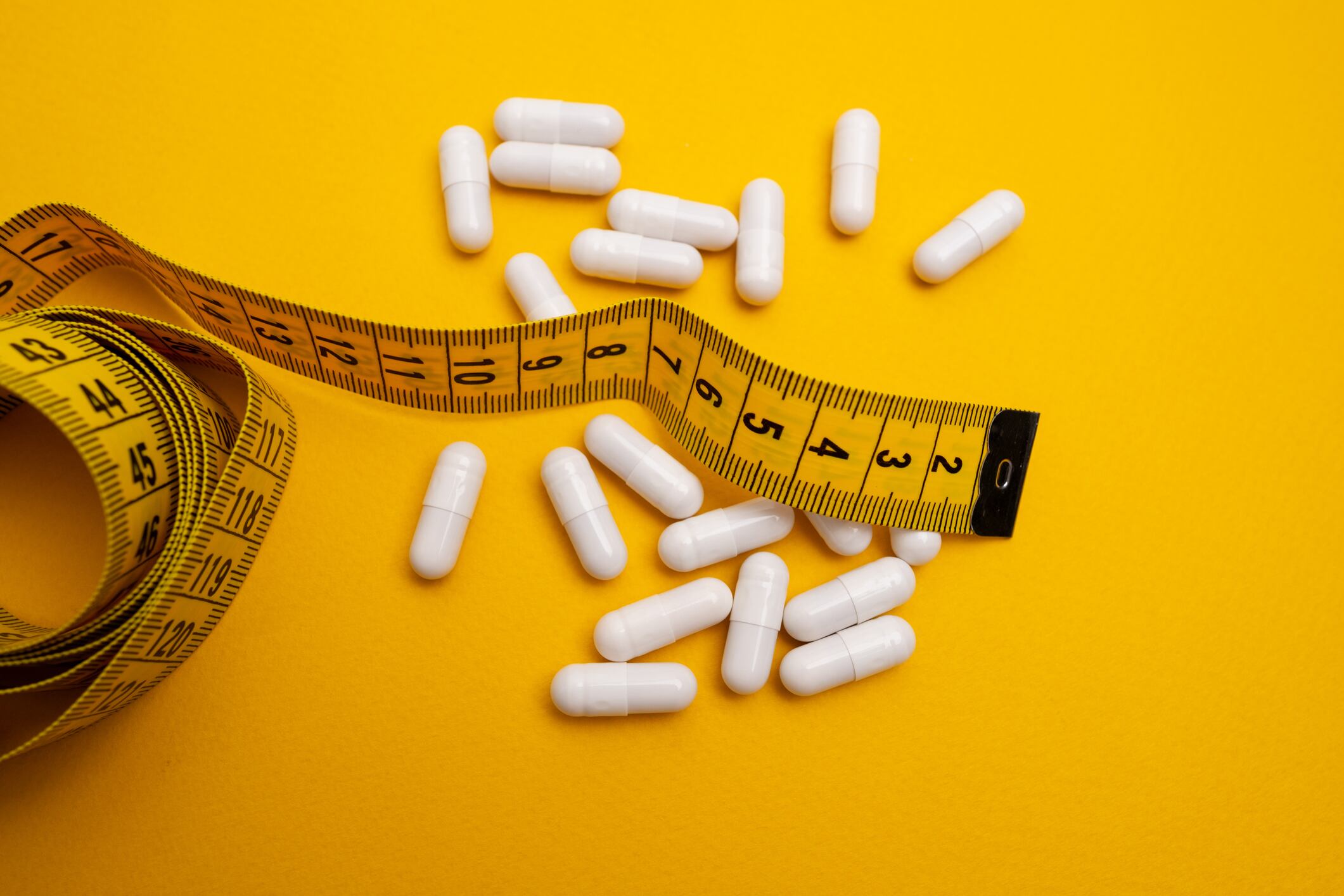 Measuring tape and tablets, vitamins on a colored background with space for text. Concept of losing weight, dieting, burning fat, healthy eating