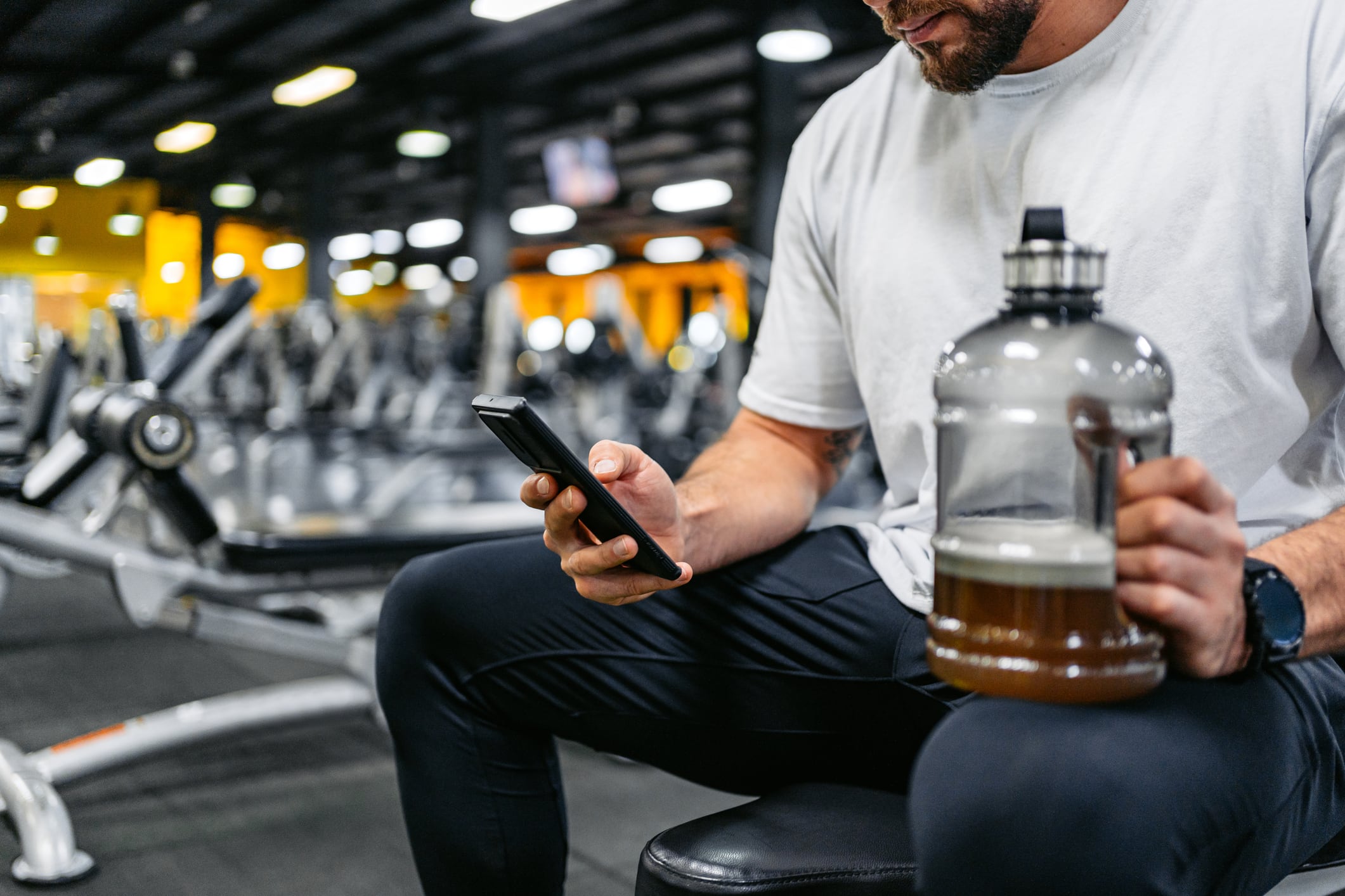 Handsome young muscular man using a phone while drinking a protein shake after training in the gym in Kuwait City.