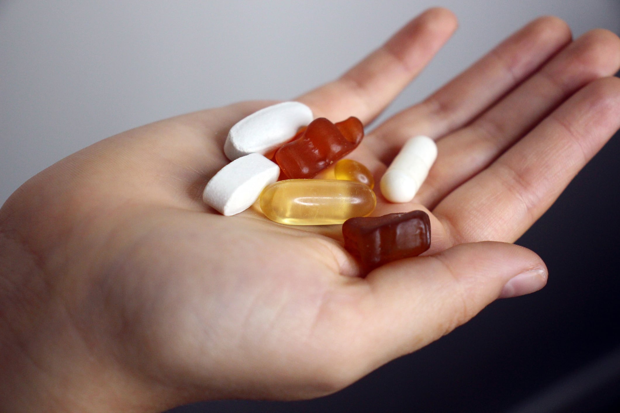 A hand holding assorted capsules, gummy vitamins, and tablets