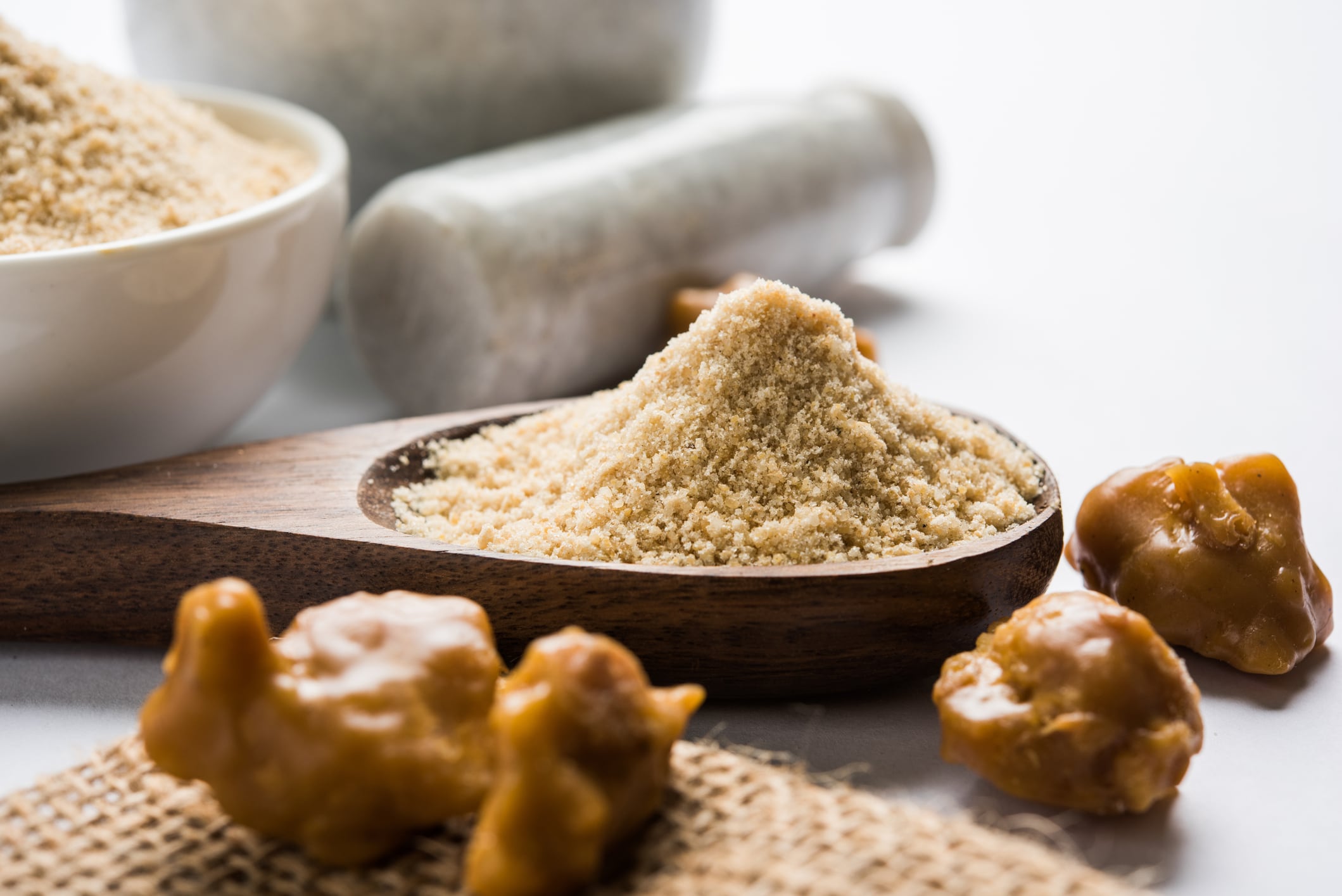 Asafoetida cake and powder or Hing or Heeng which is an important ingredient in Indian food recipes with big wooden spoon and mortar, selective focus