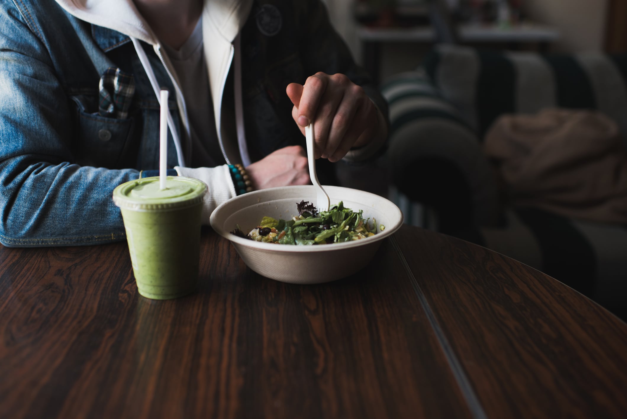 Young man sitting at table, eating salad, mid section