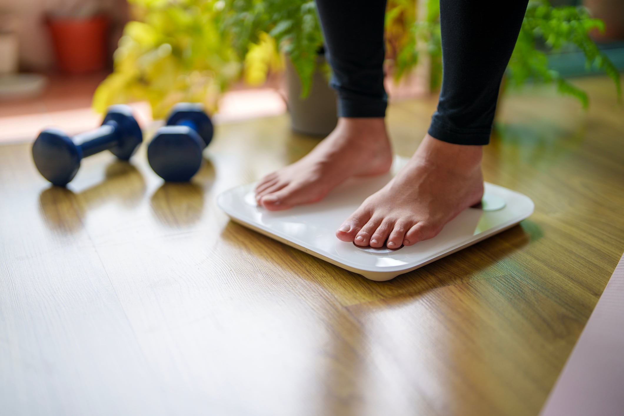 Young woman standing on a weighing scale, focusing on her feet and the display as she checks her weight