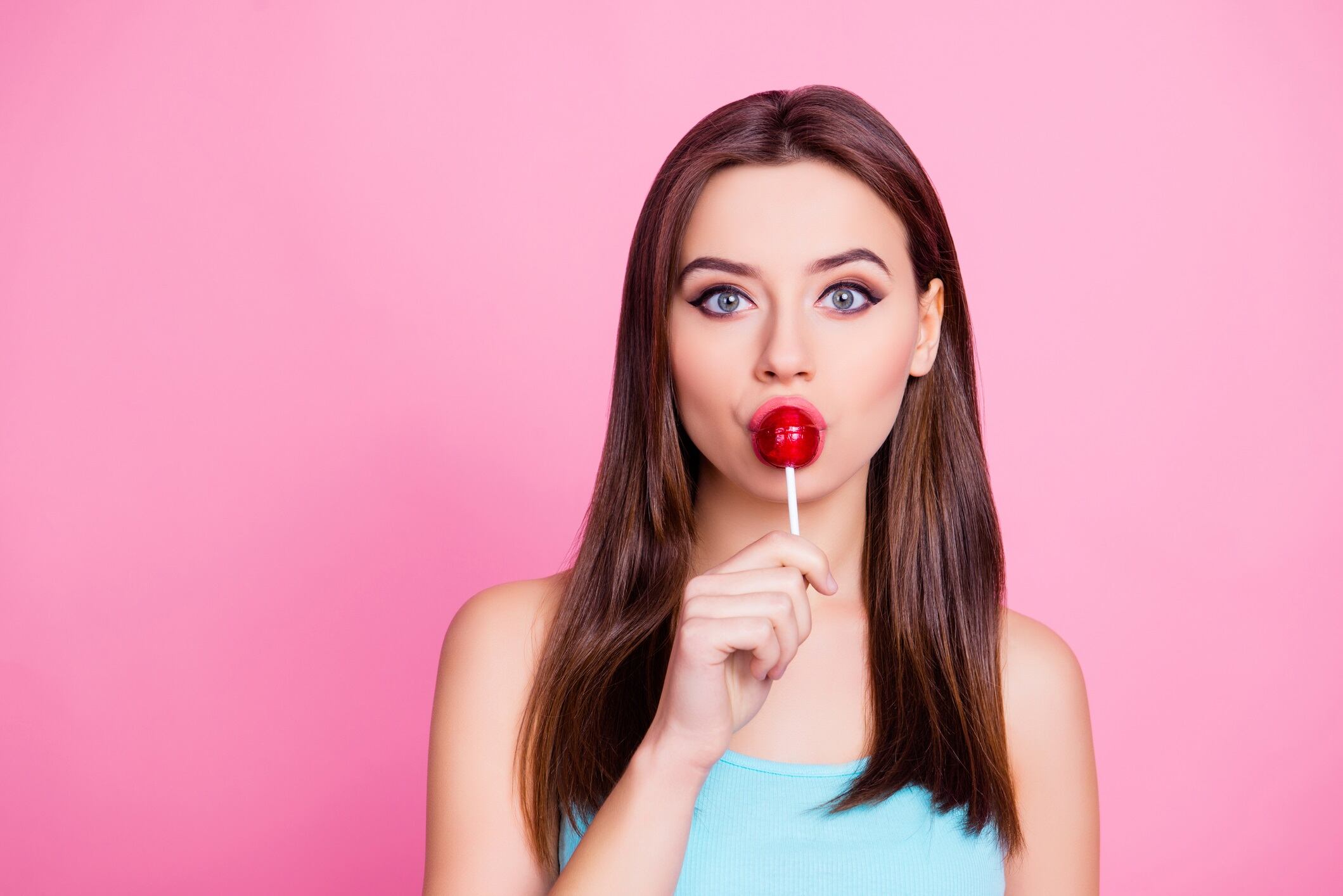 Close up portrait of girl eating red lollipop on stick isolated on pink background.