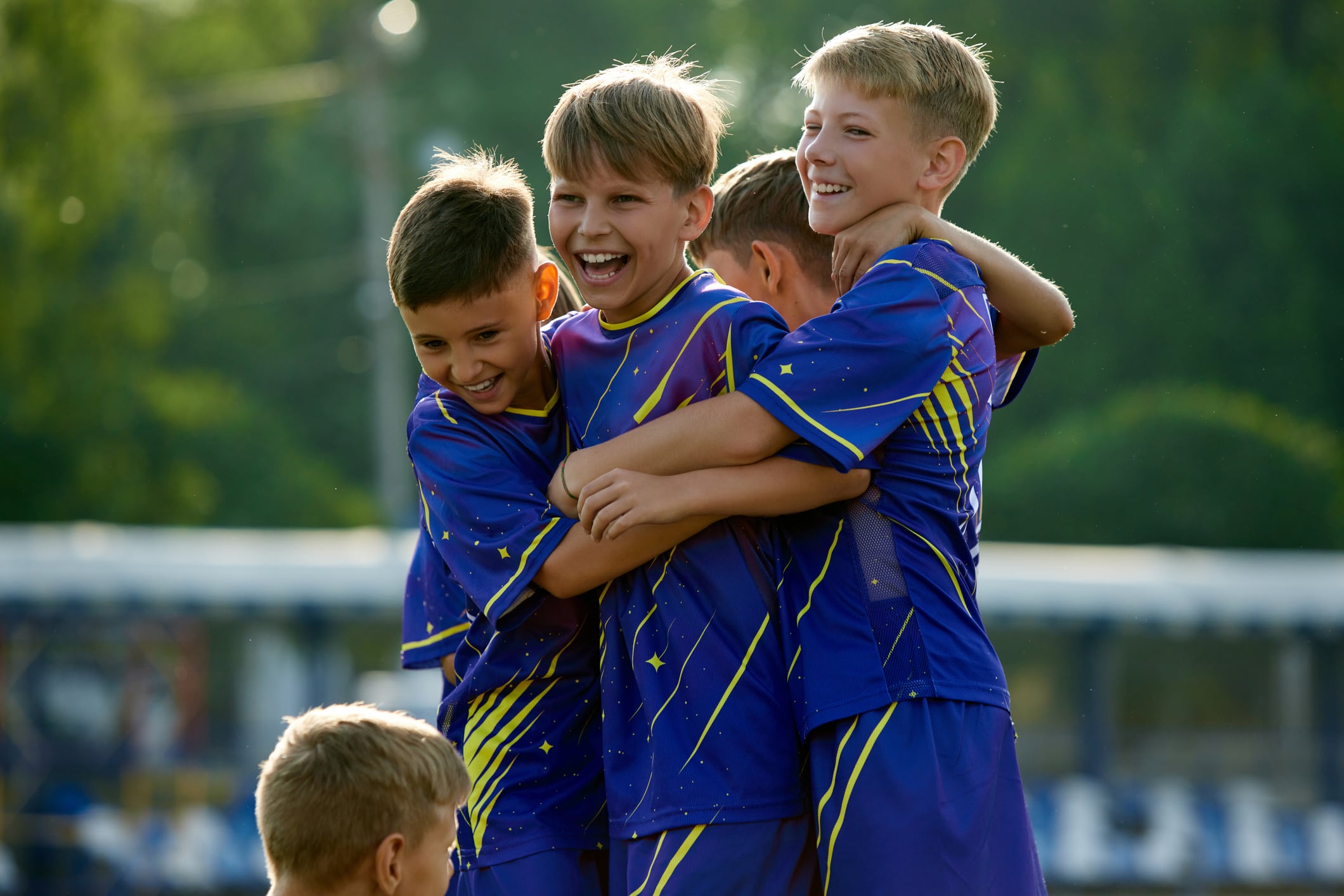 Dynamic moment of victory. Boys, friends in blue uniform, soccer players in motion, jumping and hugging, celebrating winning game. Concept of sport, childhood, education, achievement, active lifestyle