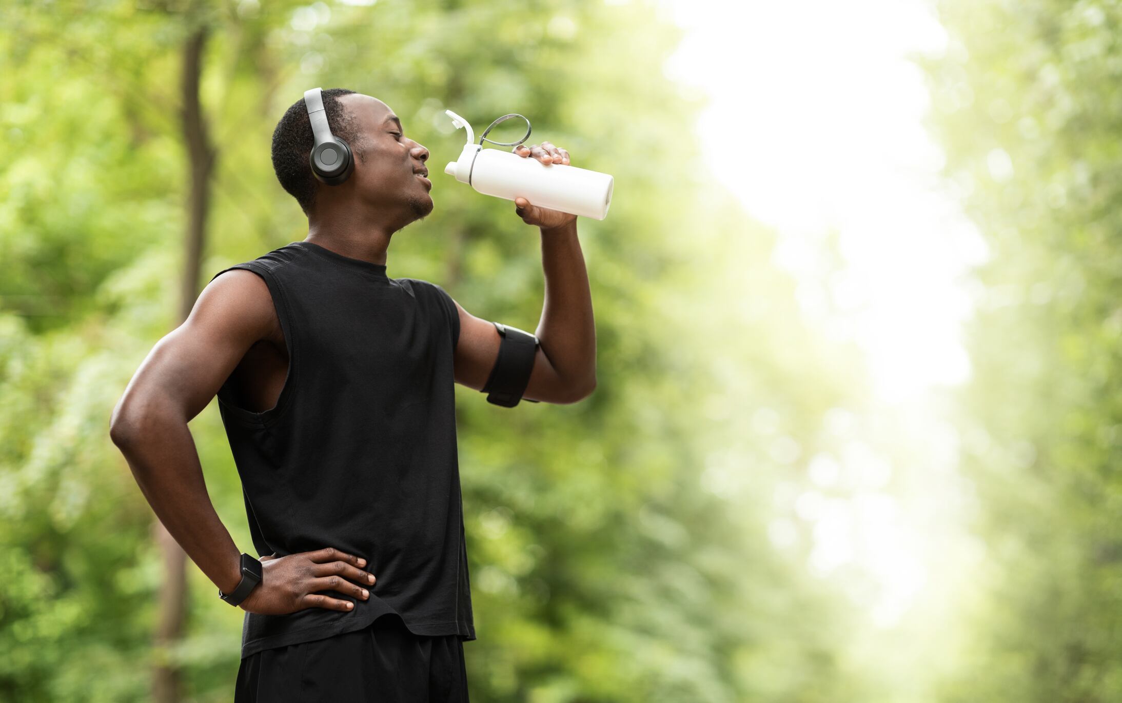 African american young sportsman drinking water, having break during exercising open air, copy space, side view