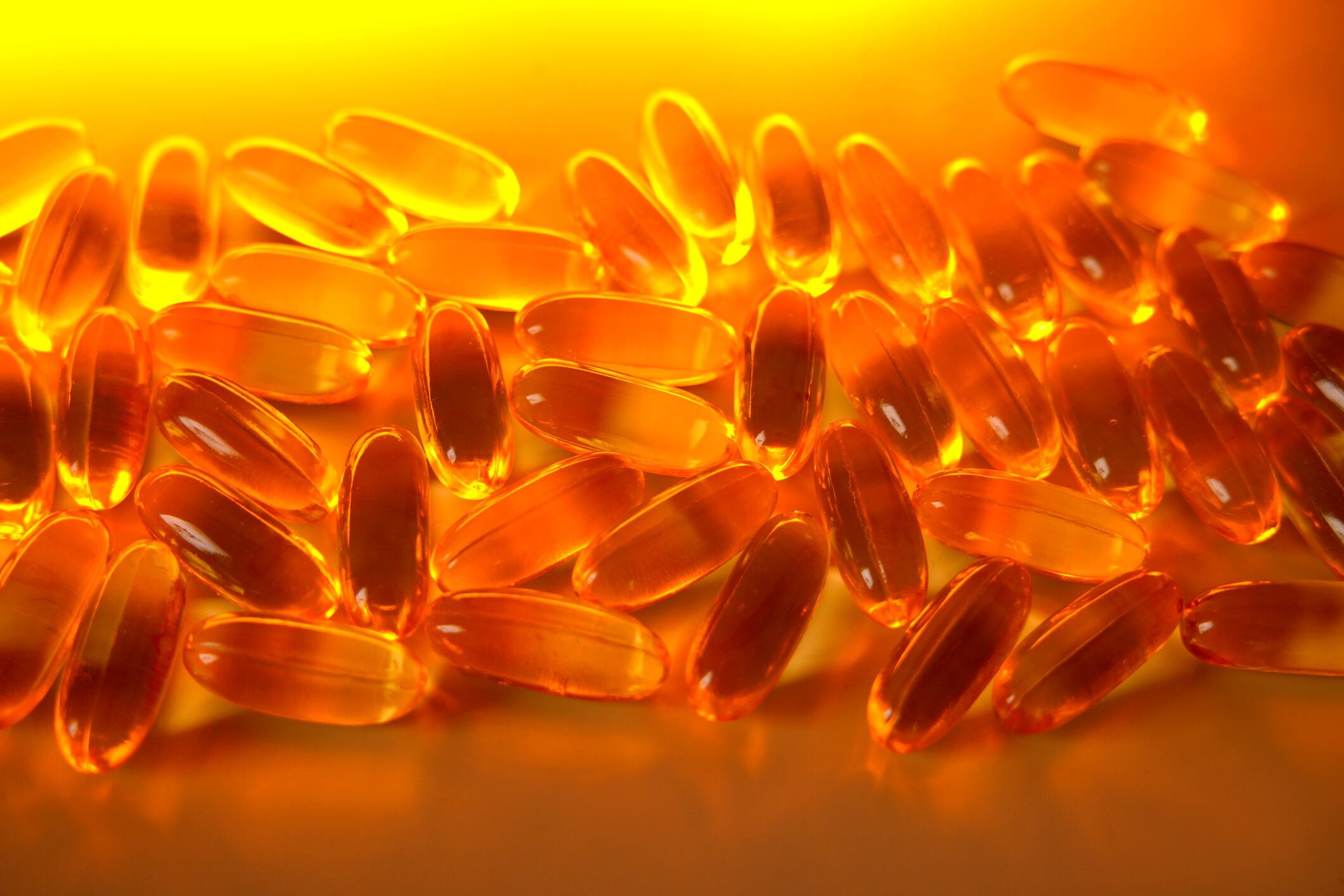 Numerous fish oil capsules, rich in omega-3 fatty acids, lie on an orange surface, promoting health and well-being
