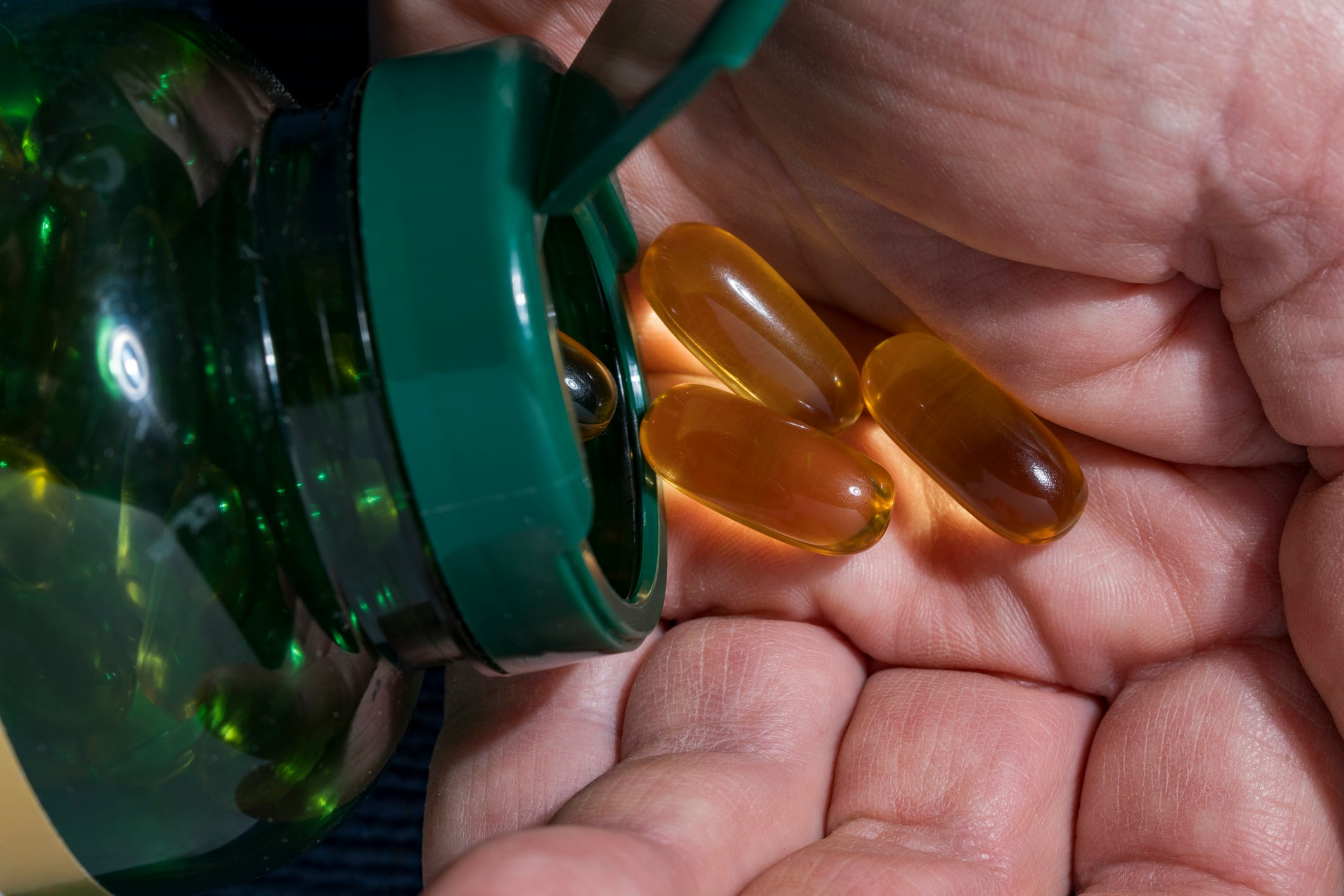 Fish oil omega 3 capsules pouring from bottle into hand. Close up of a person pouring amber softgel omega 3 or vitamin e capsules from a green plastic bottle into their hand