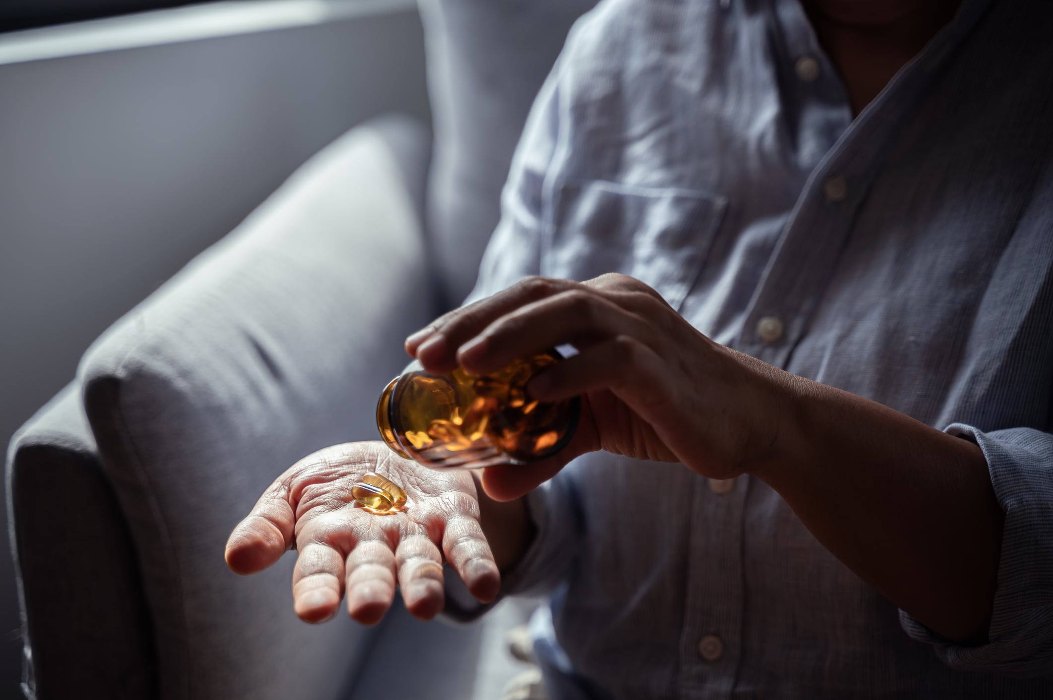 Close up hand of an elderly Asian woman is pouring vitamins from a bottle to take for boosting her immune system and nourishing her body. Senior people health care vitamin product concept.