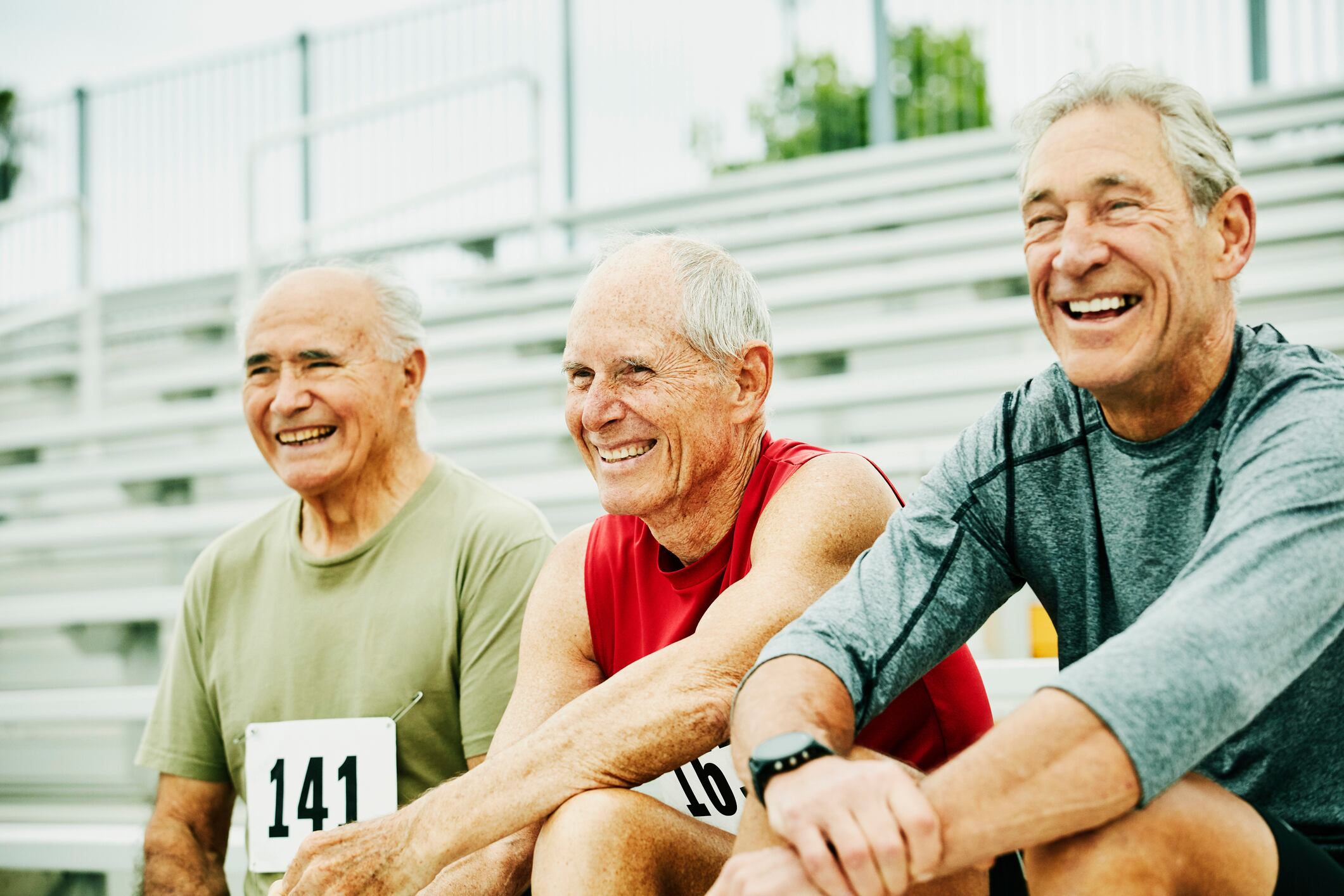 Smiling and laughing senior male track athletes hanging out together on bleachers
