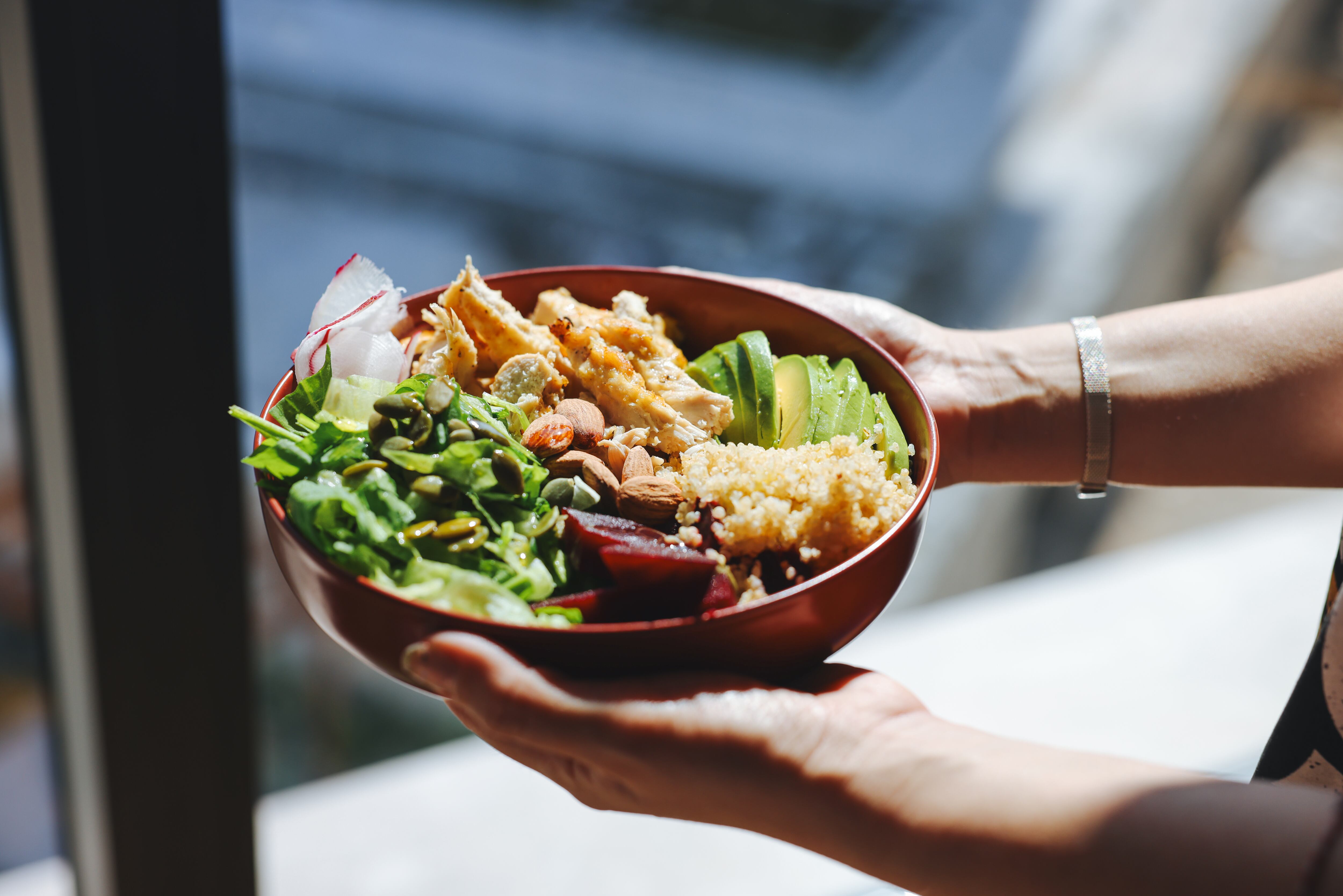 Woman holding a bowl of salad with grains, protein, and greens