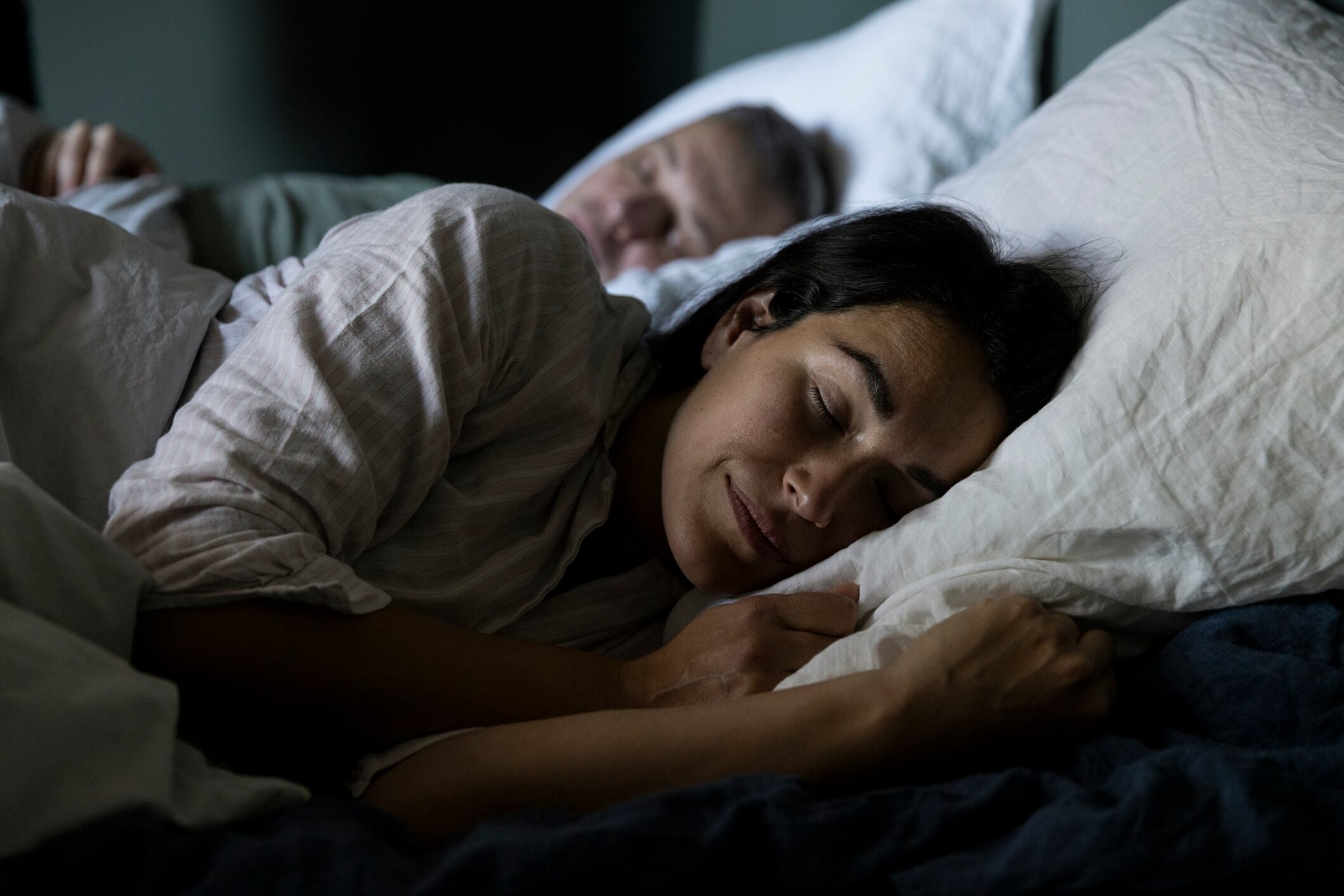 Woman sleeping in bed, man beside her, bedroom at home