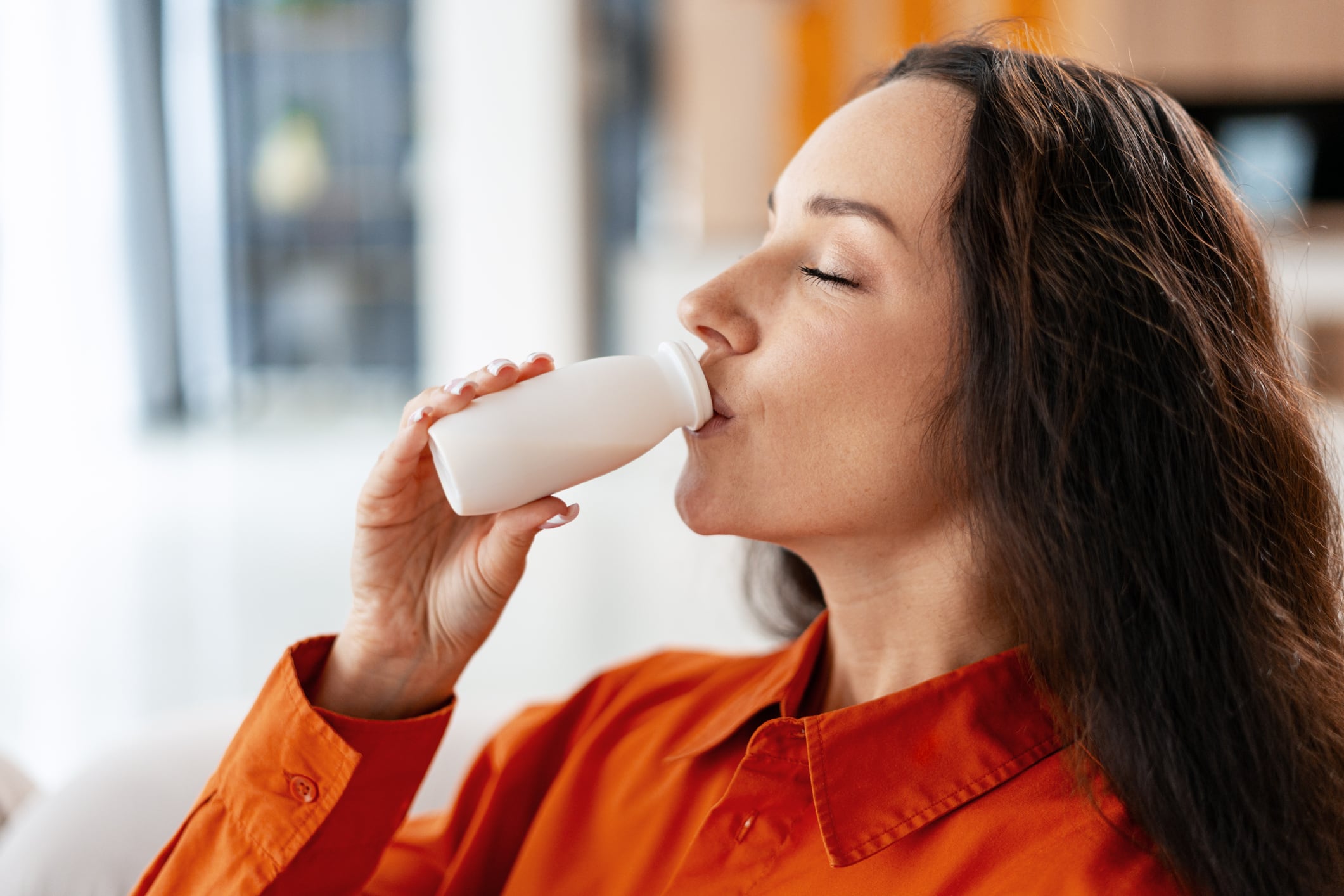 Woman drinking a small bottle of yogurt, focusing on the healthy benefits and enjoyment of probiotics and dairy nutrition