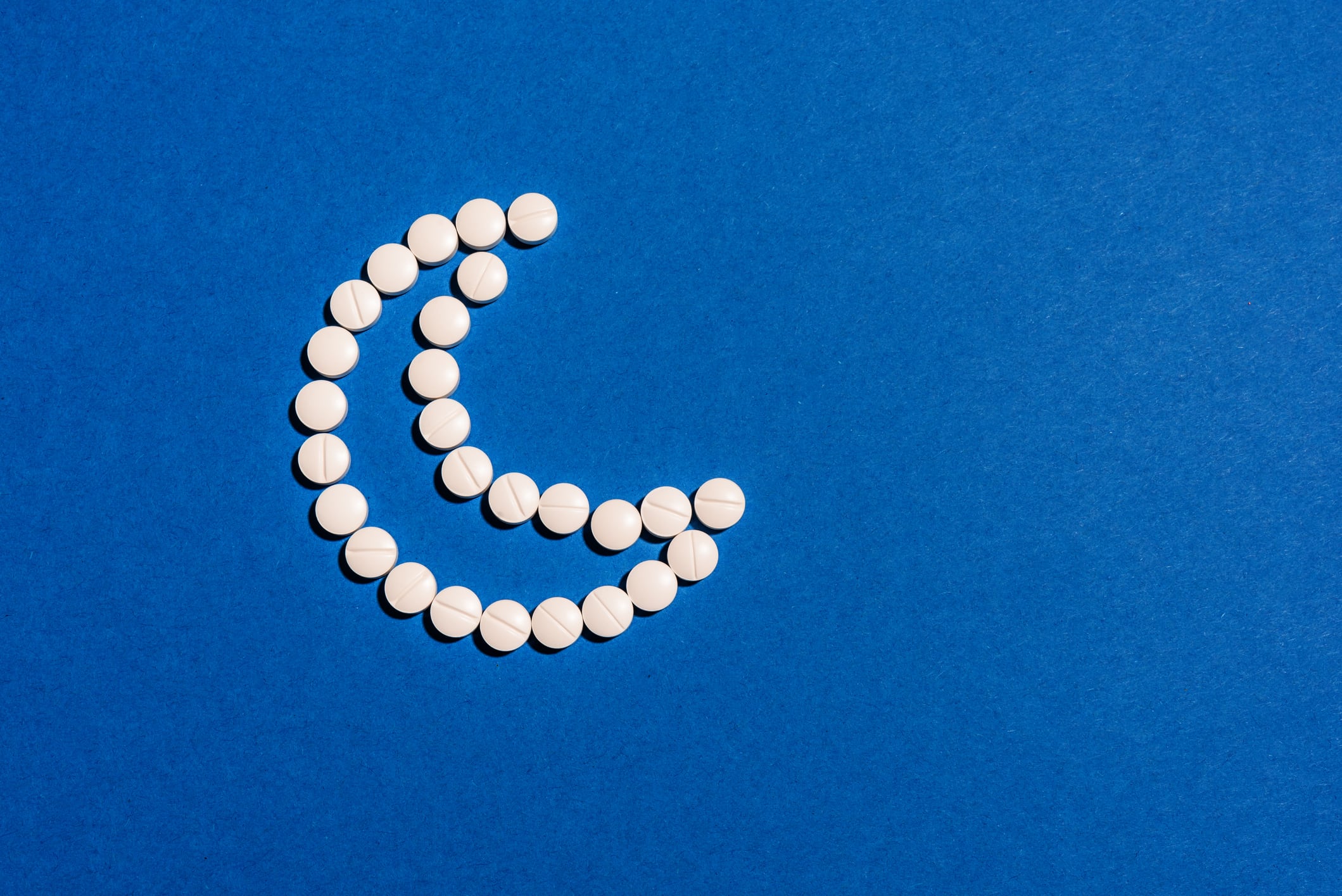 White melatonin pills in shape of crescent moon on dark blue background. Insomnia, healthy sleeping, daily supplements concept.