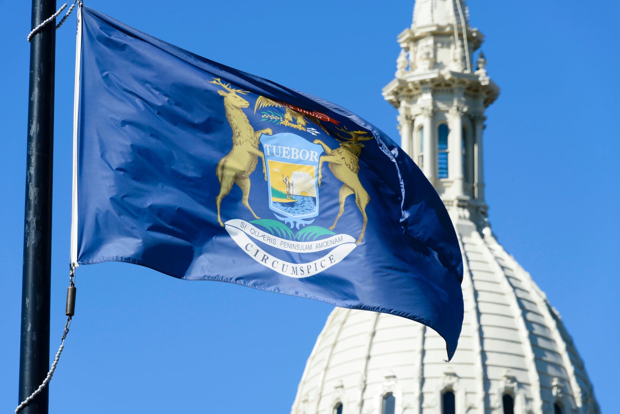 Michigan flag waving in front of the beautiful dome of the Capitol Building in downtown Lansing, the capital of Michigan.