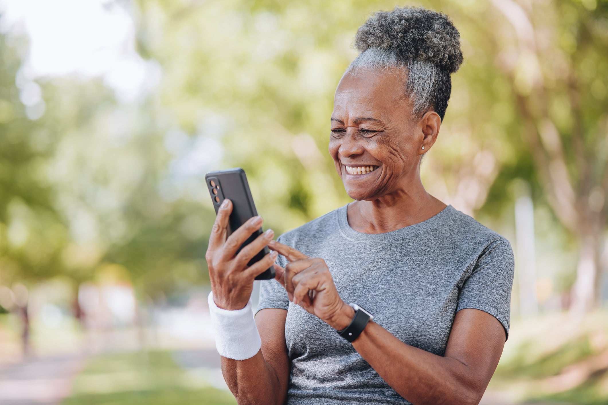 Senior woman of African ancestry smiles at phone in open green park