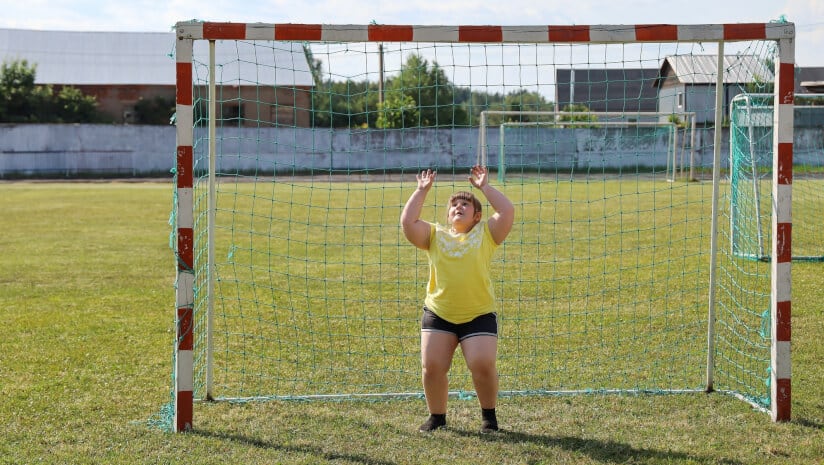 An overweight/obese child standing in a goal getting ready to catch a soccer ball.