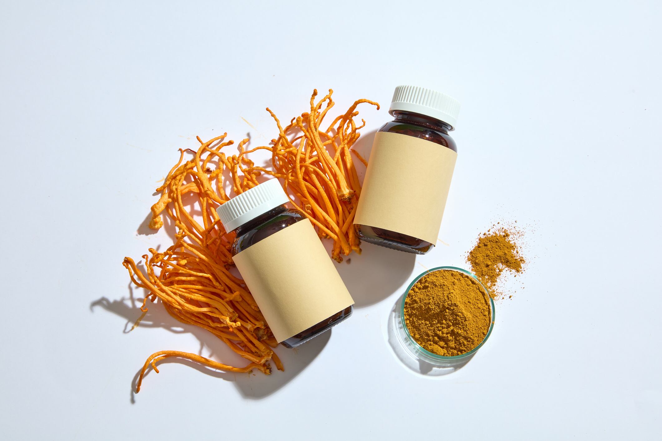 A glass petri dish full of Cordyceps powder. Two glass bottles of medicine decorated with Cordyceps Militaris. Cordyceps may boost exercise performance