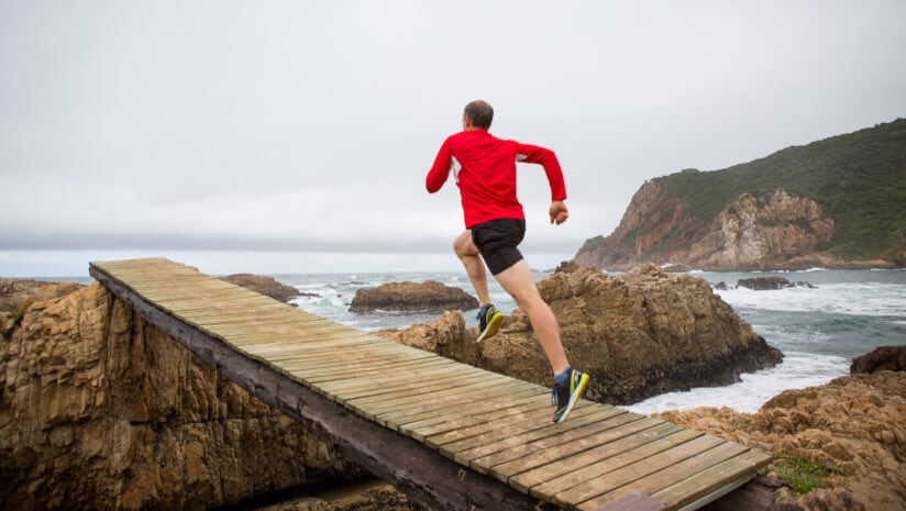 Performance runner running across a plank walkway to the ocean