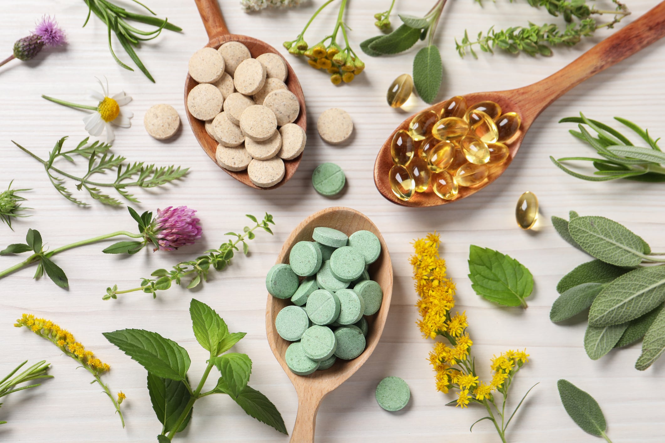Different pills, herbs and flowers on white wooden table, flat lay. Dietary supplements
