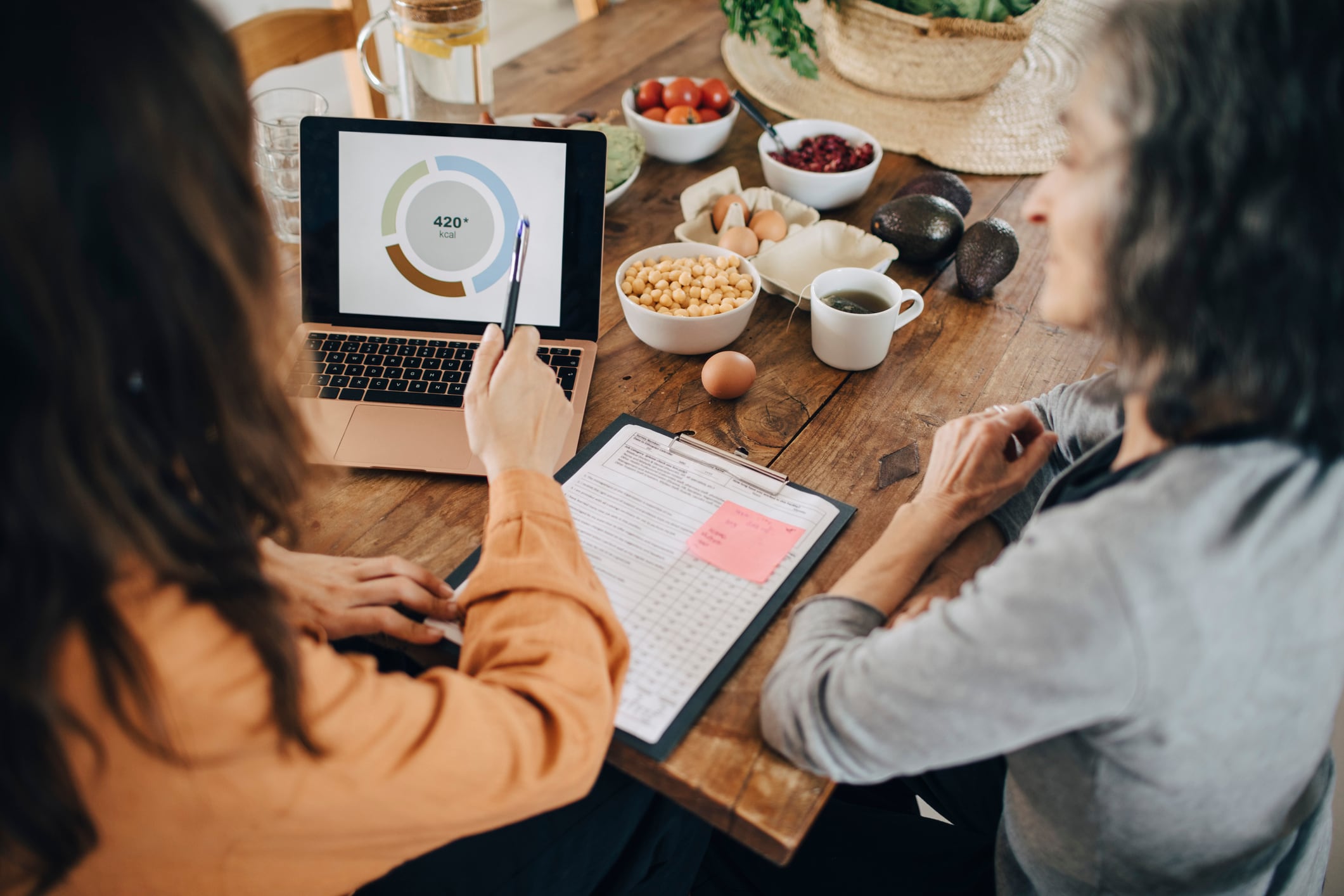 Female nutritionist explaining senior woman over laptop at dining table