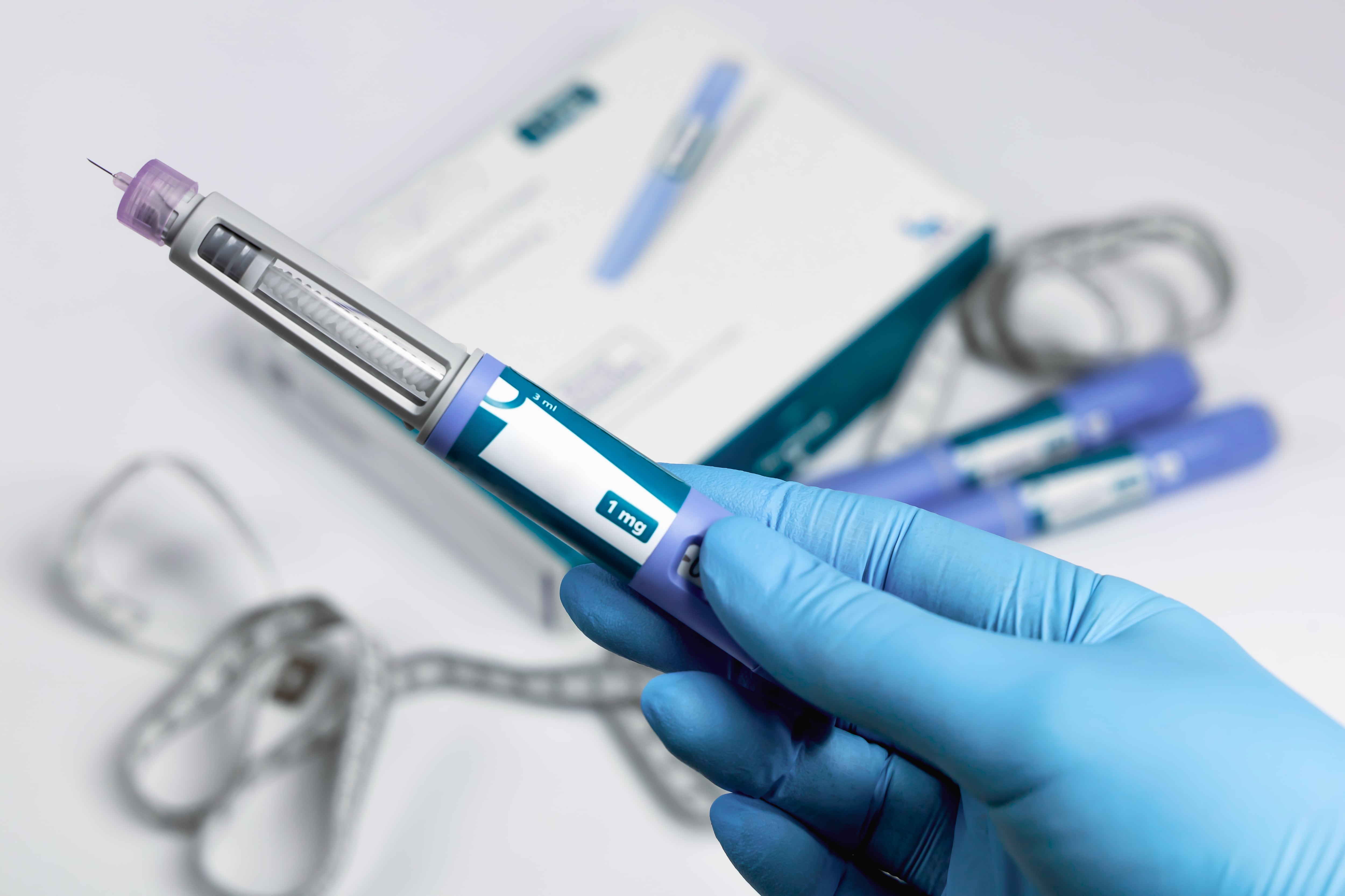 Hands in blue surgical gloves holding Ozempic Insulin injection pen for diabetics.