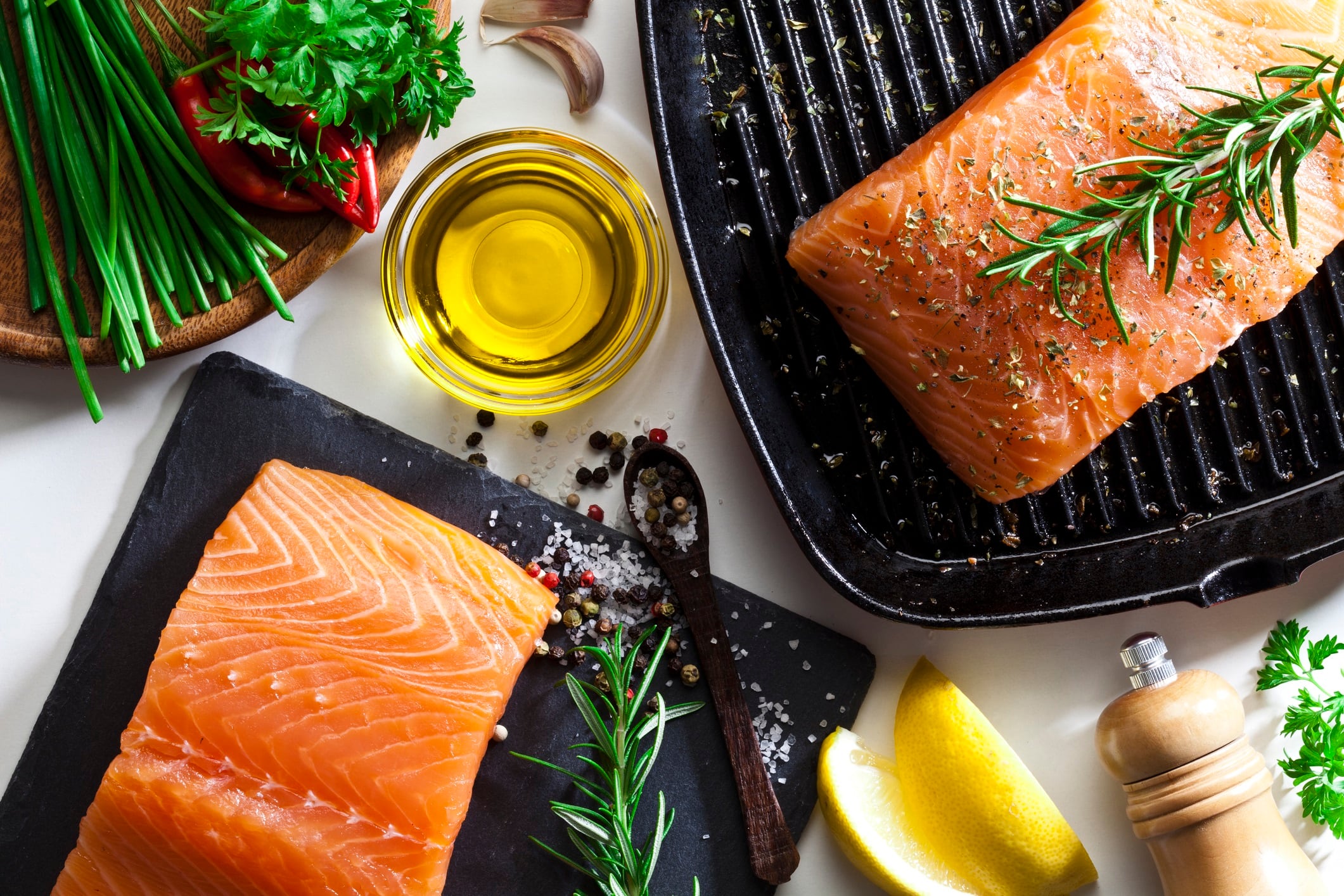 Top view of two raw salmon steaks ready for cooking. Some ingredients for cooking salmon like salt, pepper, rosemary, chive, lime and olive oil are all around the frame.