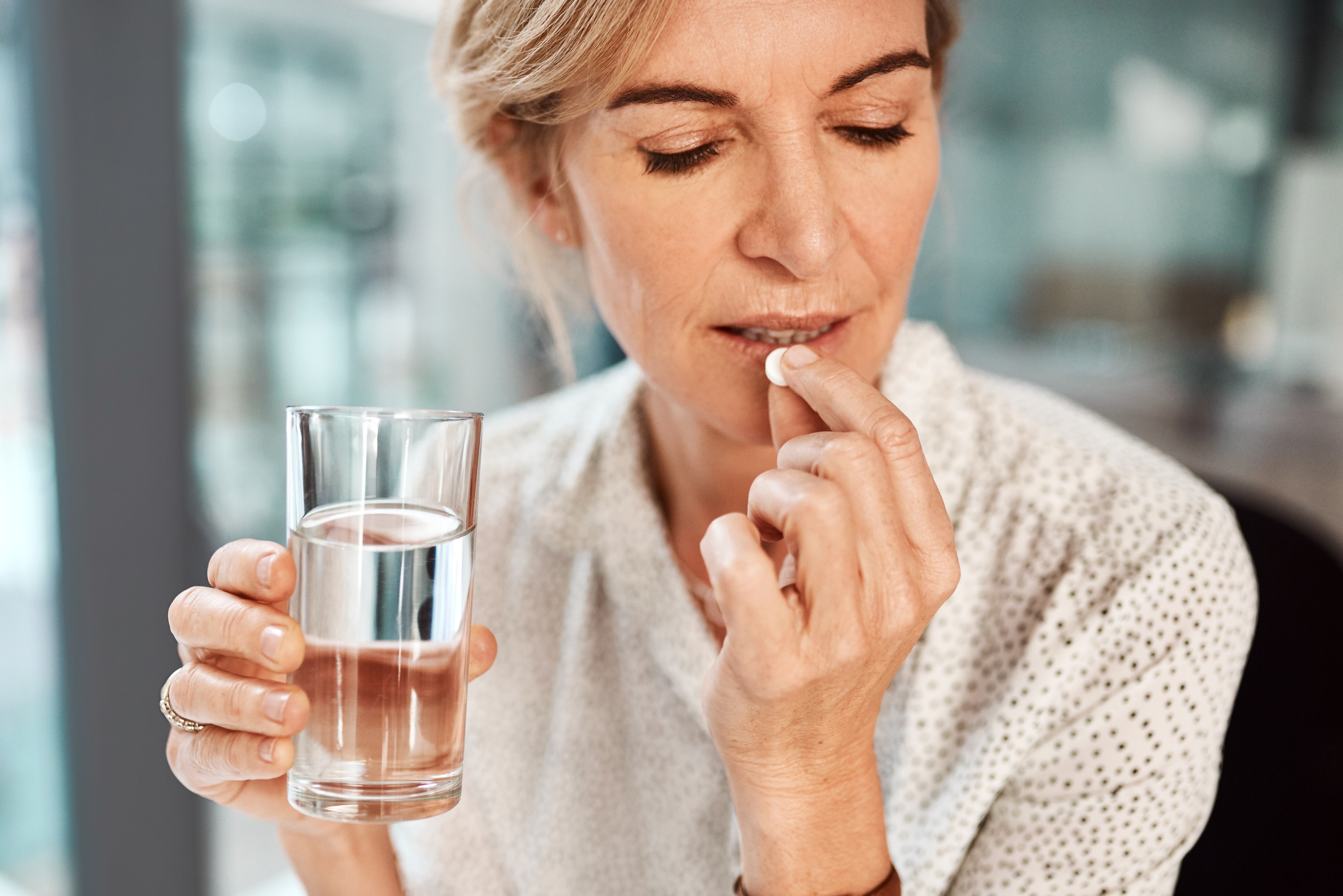 Middle-aged woman taking a white pill with a glass of water