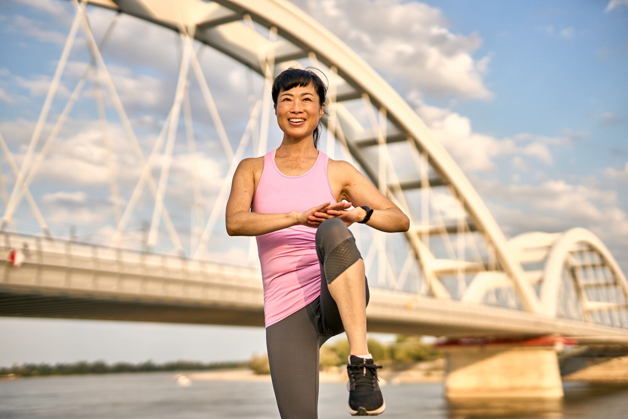 Mid adult asian sportswoman exercise outdoor by the river with a bridge in the background