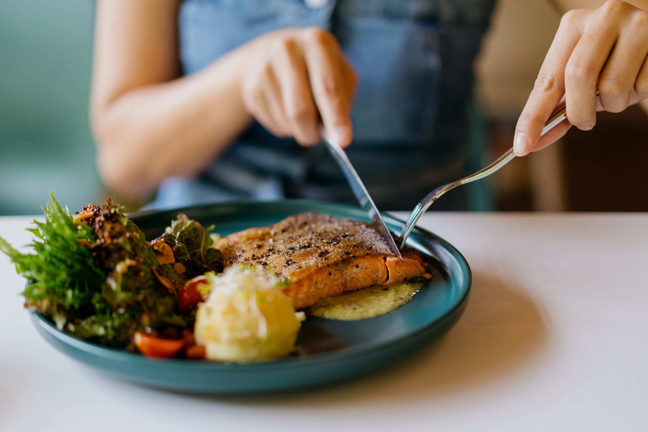 Close up shot of a woman eating pan fried salmon with table knife and fork in cafe