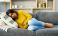 A woman with stomach cramps resting on the sofa. © Getty Images